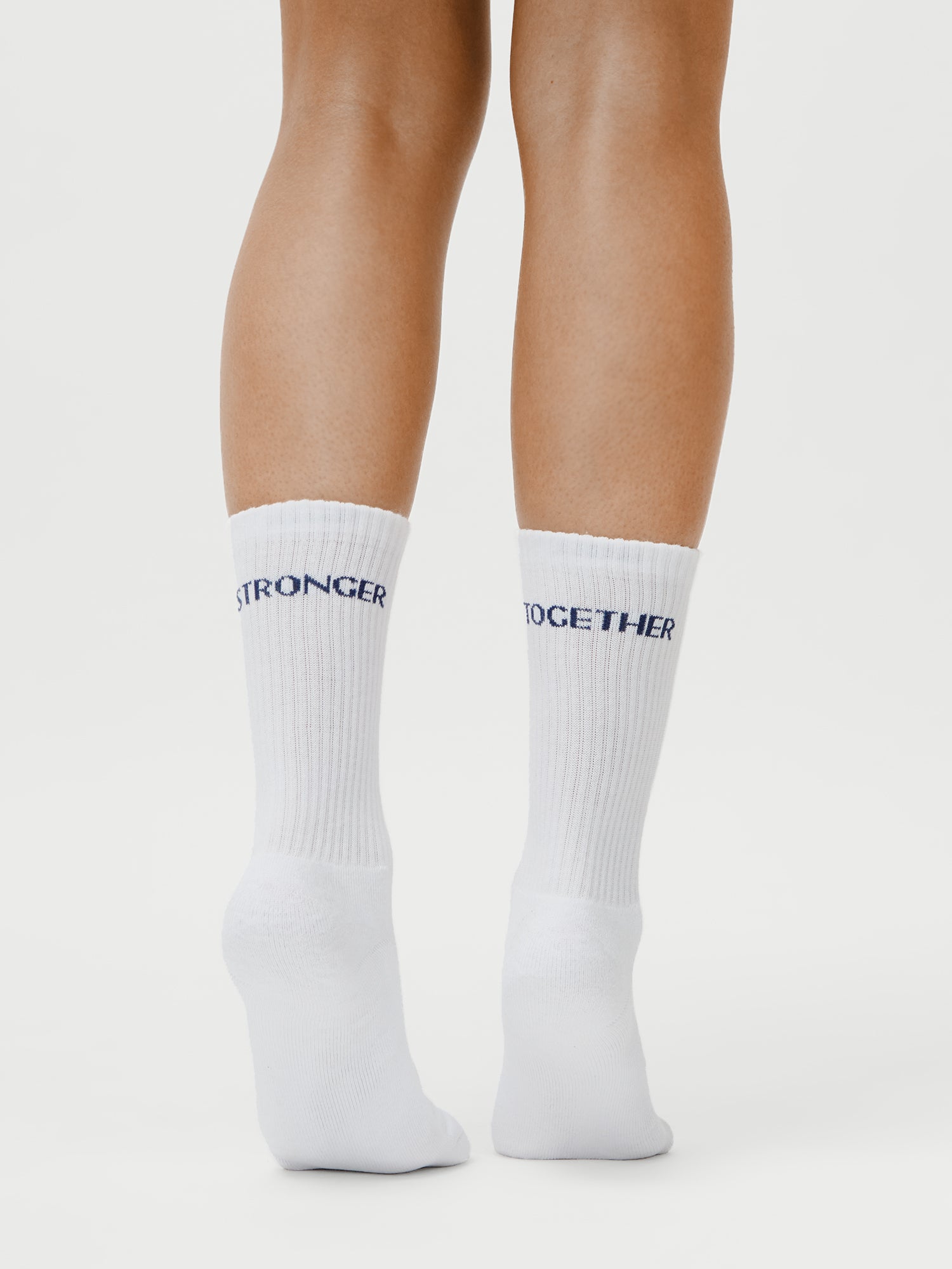 Eine Person (1,73m, Größe 36) steht auf Zehenspitzen in weißen LeGer x Oh April - Sue Socks Stronger by LeGer von Lena Gercke, mit "STRONGER TOGETHER" in blau auf der Rückseite. Einfacher weißer Hintergrund. Produktinformation auf Anfrage erhältlich.