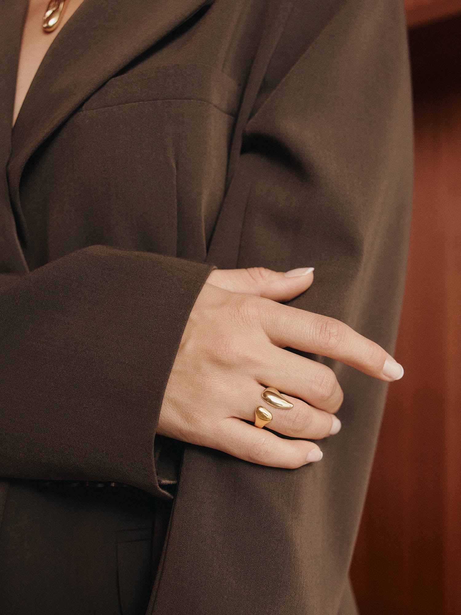 Eine Person in einem braunen Blazer verschränkt die Arme und trägt den LeGer x Purelei - Freedom Ring by LeGer by Lena Gercke am Finger. Ihre Nägel sind ordentlich manikürt und mit hellem Lack lackiert.