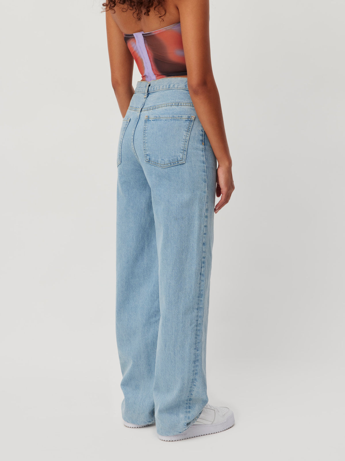 Rückansicht der hoch taillierten Carla-Hose aus blauem Denim in heller Waschung mit weitem Bein.