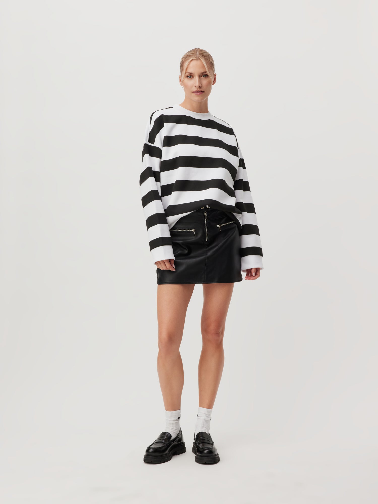 Ein Model trägt das Sweatshirt „Vanessa“ von LeGer by Lena Gercke, kombiniert es mit einem schwarzen Lederrock, weißen Socken und schwarzen Schuhen vor einem schlichten Hintergrund und zeigt so die perfekte Passform.