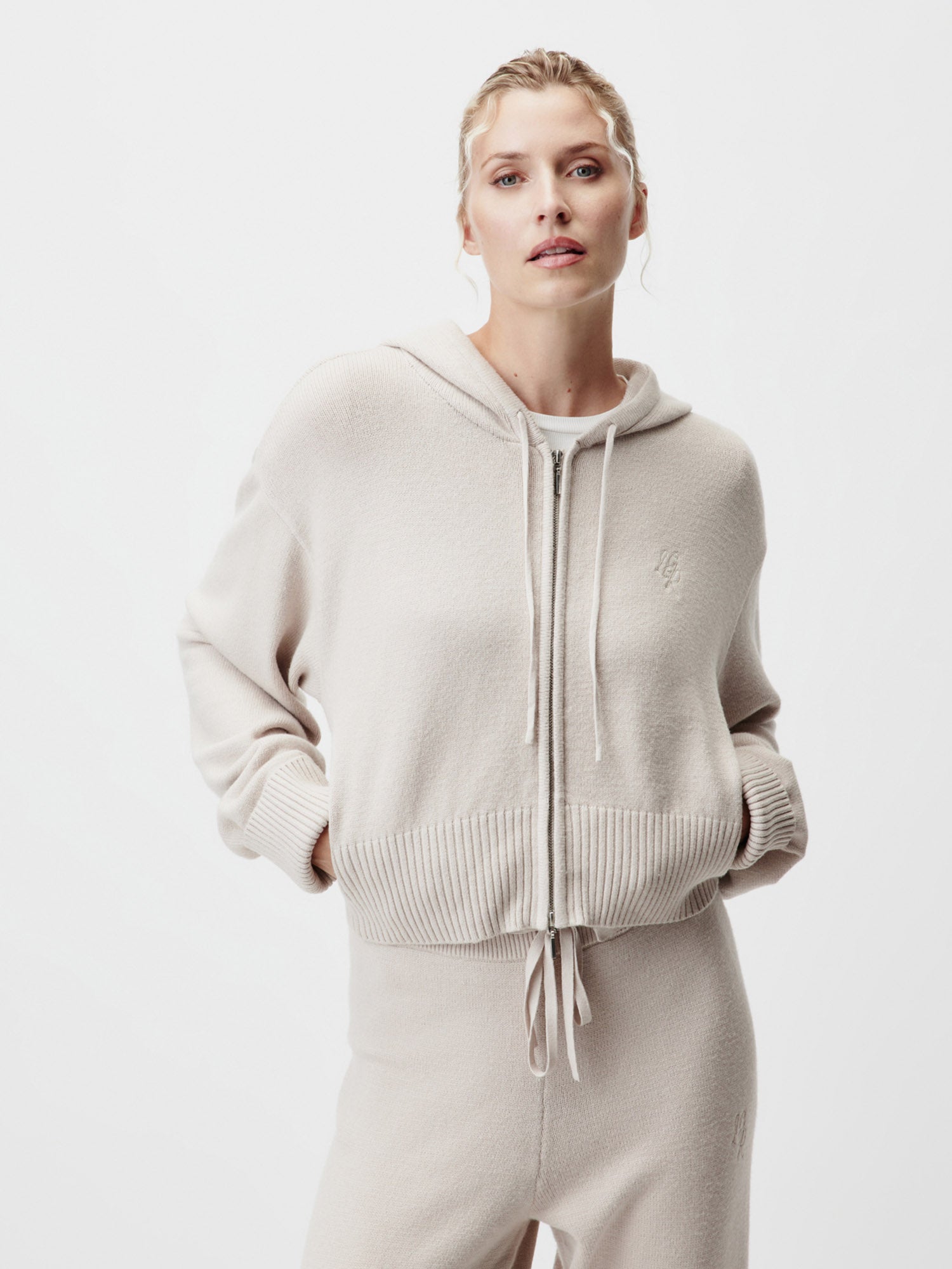 Eine Person steht vor einem weißen Hintergrund und trägt die LeGer by Lena Gercke Cornelia Strickjacke in Größe 36 mit gerippten Bündchen und Saum sowie eine passende Hose. Ihre Hände stecken in den Taschen der Strickjacke, während sie in die Kamera schaut.