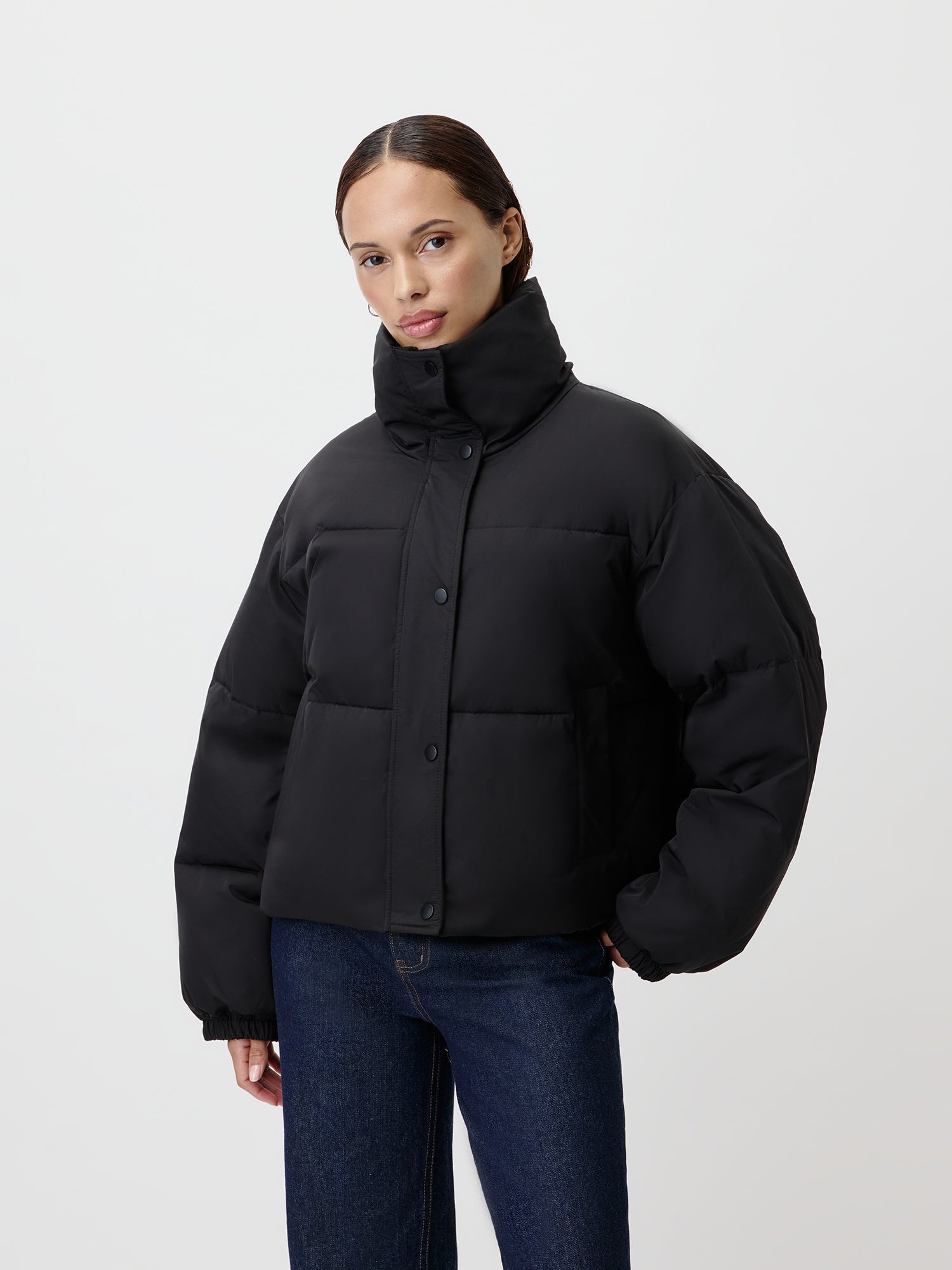 Eine Person in der Duffy-Jacke von LeGer by Lena Gercke steht vor einem schlichten weißen Hintergrund. Die Hände in den Jackentaschen verstaut, strahlt sie in dunklen Jeans und einem kuscheligen Langarmshirt darunter eine lässige Ausstrahlung aus.