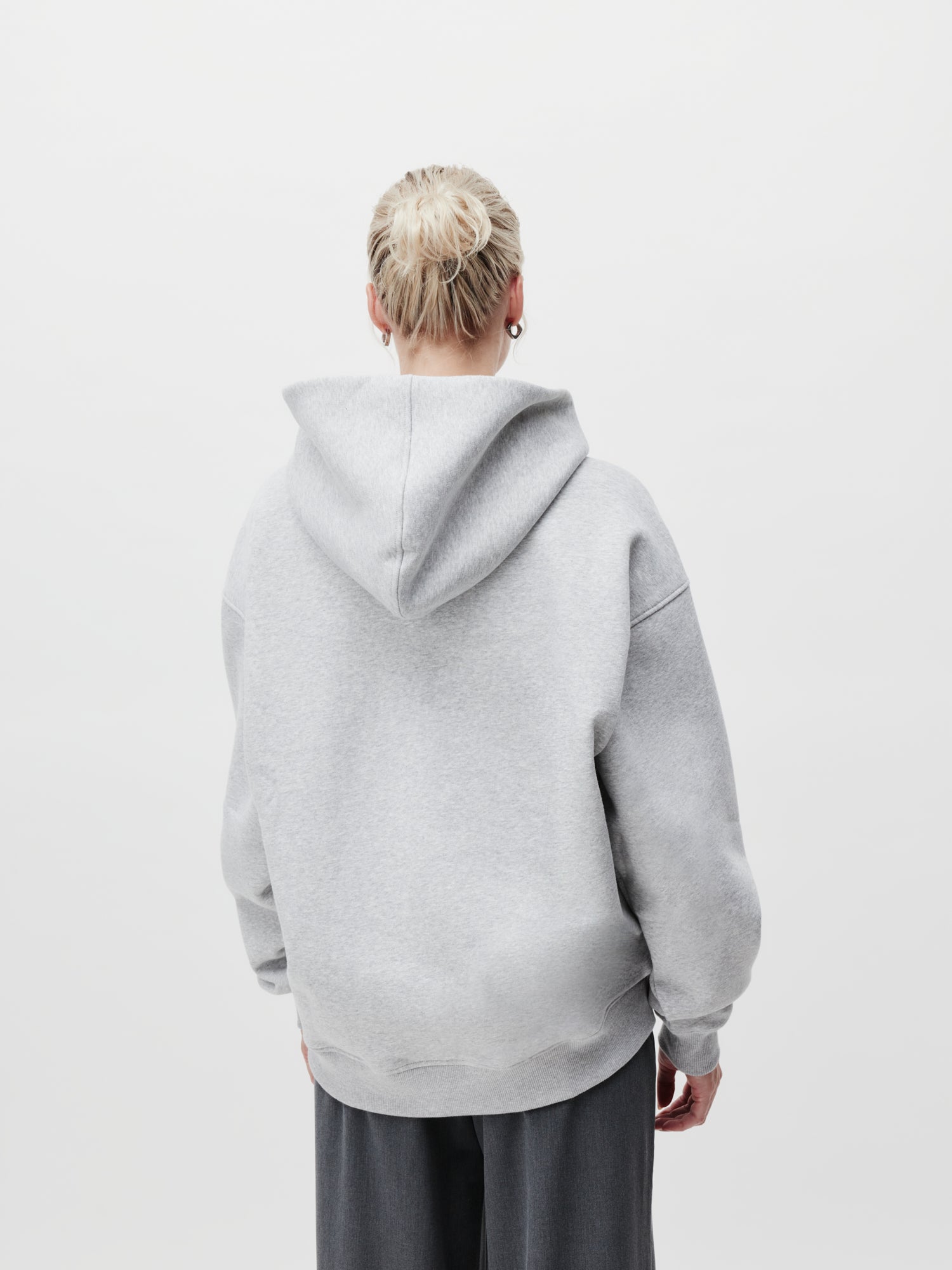 Eine Person mit hochgesteckten blonden Haaren trägt einen grauen Abby Hoodie von LeGer by Lena Gercke und eine dunkle Hose und steht mit dem Rücken zur Kamera vor einem schlichten weißen Hintergrund. Der Hoodie hat lange Ärmel und passt perfekt in Größe 36.