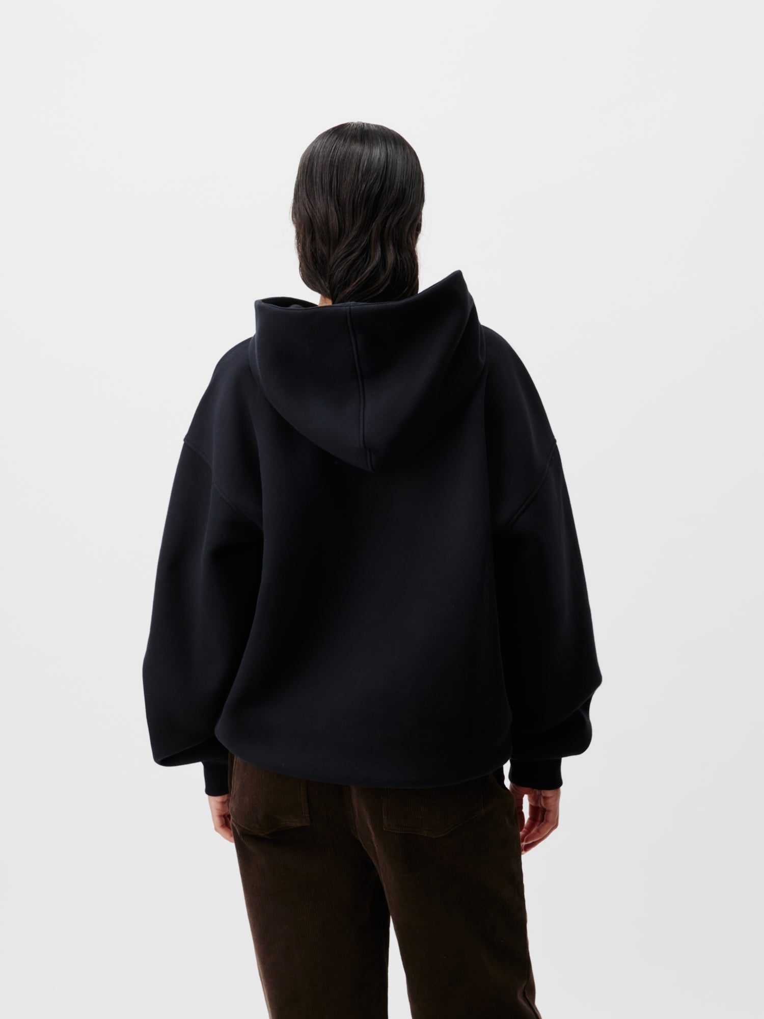 Eine Person mit langen dunklen Haaren steht mit dem Rücken zur Kamera und trägt einen Abby Hoodie von LeGer by Lena Gercke in Größe 36 und eine braune Hose vor einem schlichten weißen Hintergrund.