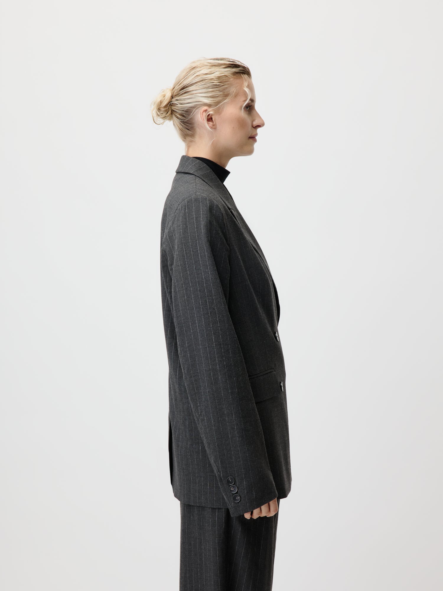 Im LeGer by Lena Gercke Delphine Blazer in Größe 36 steht eine Person mit blondem Dutt und schwarzem Langarm-Rollkragenpullover im Profil vor einem schlichten, hellen Hintergrund.
