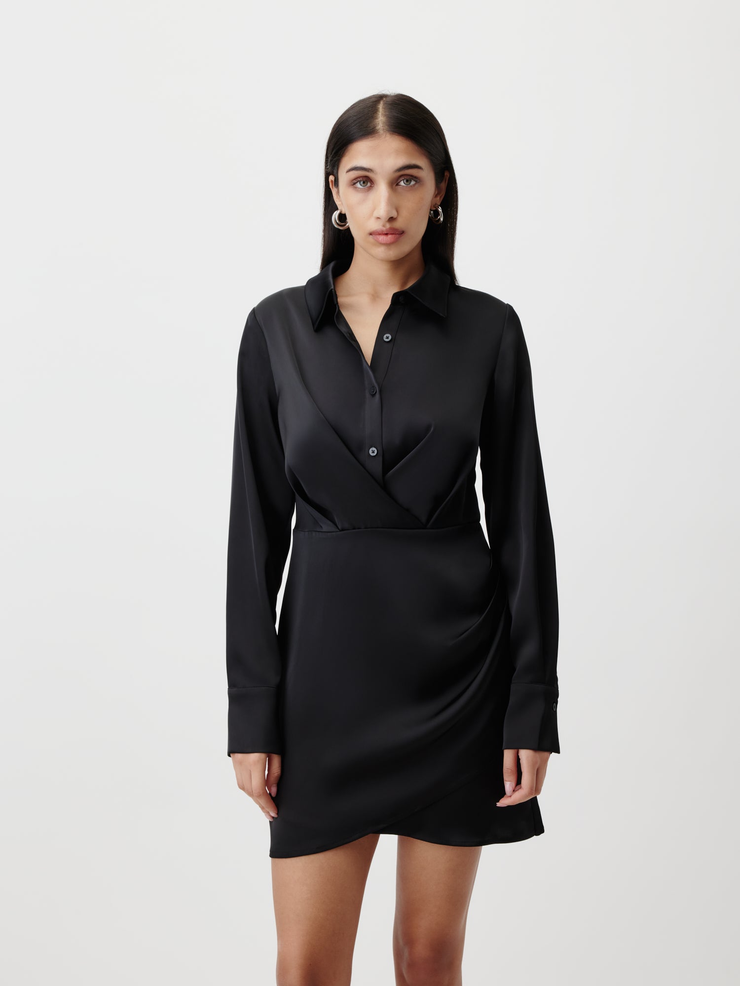 Eine Frau mit langen dunklen Haaren trägt das LeGer by Lena Gercke Dress Model "Braelyn" von LeGer by Lena Gercke - ein schwarzes, langärmeliges Wickel-Mini-Shirt-Kleid - vor einem schlichten weißen Hintergrund und blickt mit neutralem Blick in die Kamera.