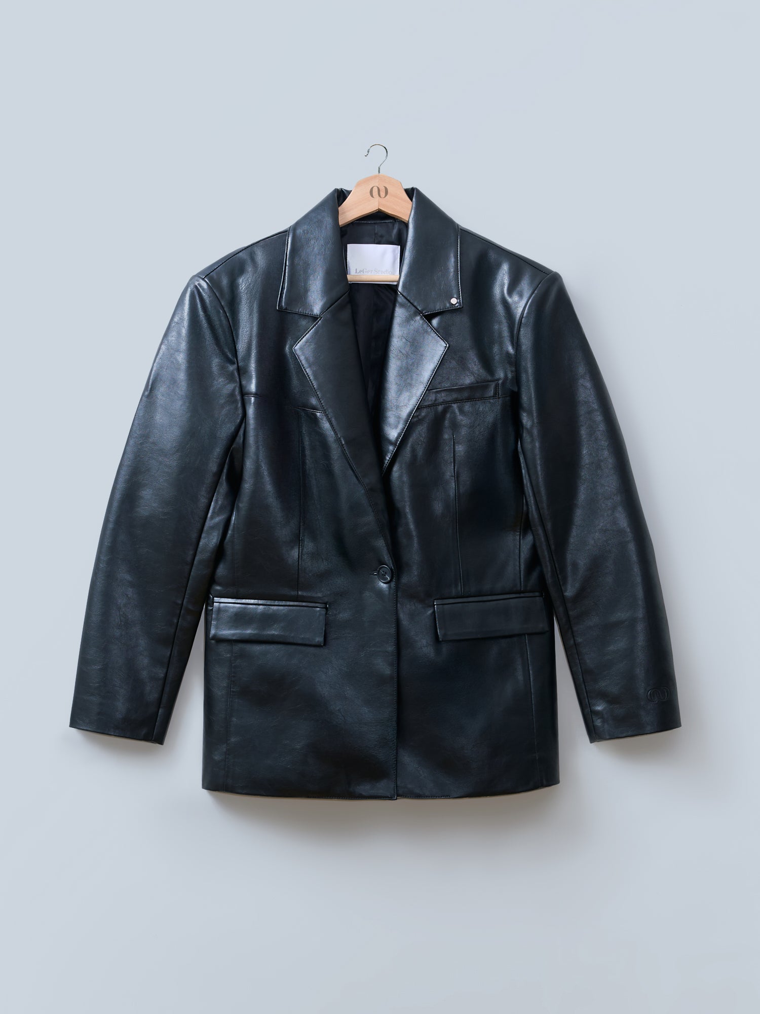 Der „Insa“-Blazer von LeGer by Lena Gercke: schwarzer Lederblazer mit einreihigem Design, taillierter Passform, gekerbtem Revers, Brust- und Vordertaschen, präsentiert auf einem Holzbügel vor hellgrauem Hintergrund.