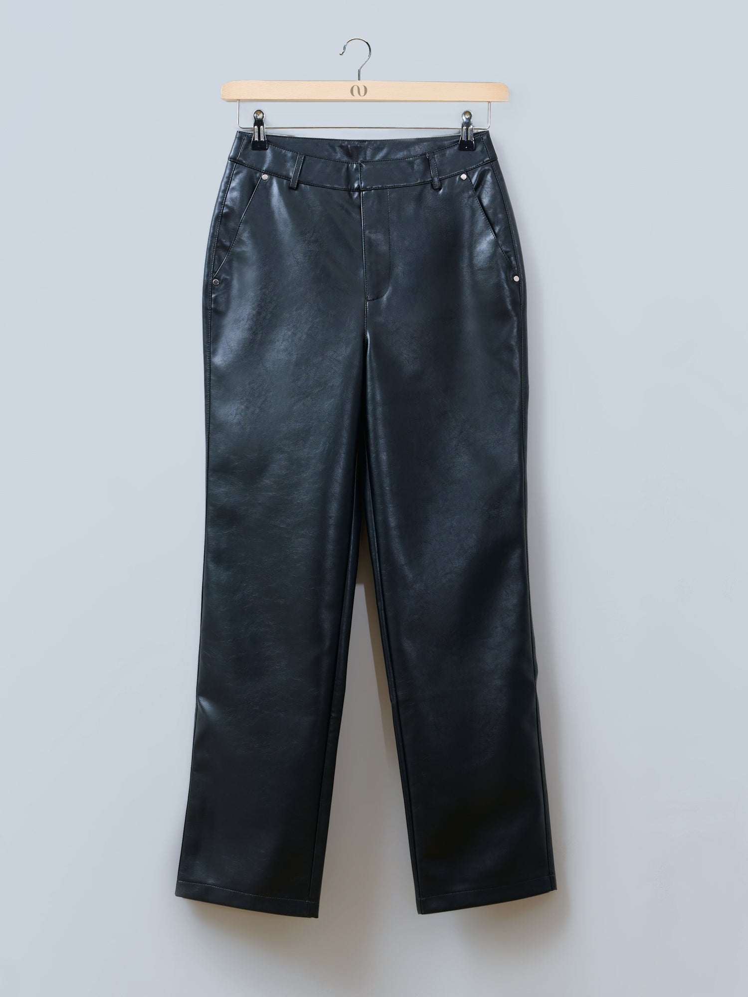 Die Hose „Insa“ von LeGer by Lena Gercke besteht aus schwarzem Kunstleder, hat eine hohe Taille, gerade Hosenbeine, Gürtelschlaufen und Seitentaschen. Abgebildet auf einem hellen Holzbügel vor einem schlichten hellgrauen Hintergrund.