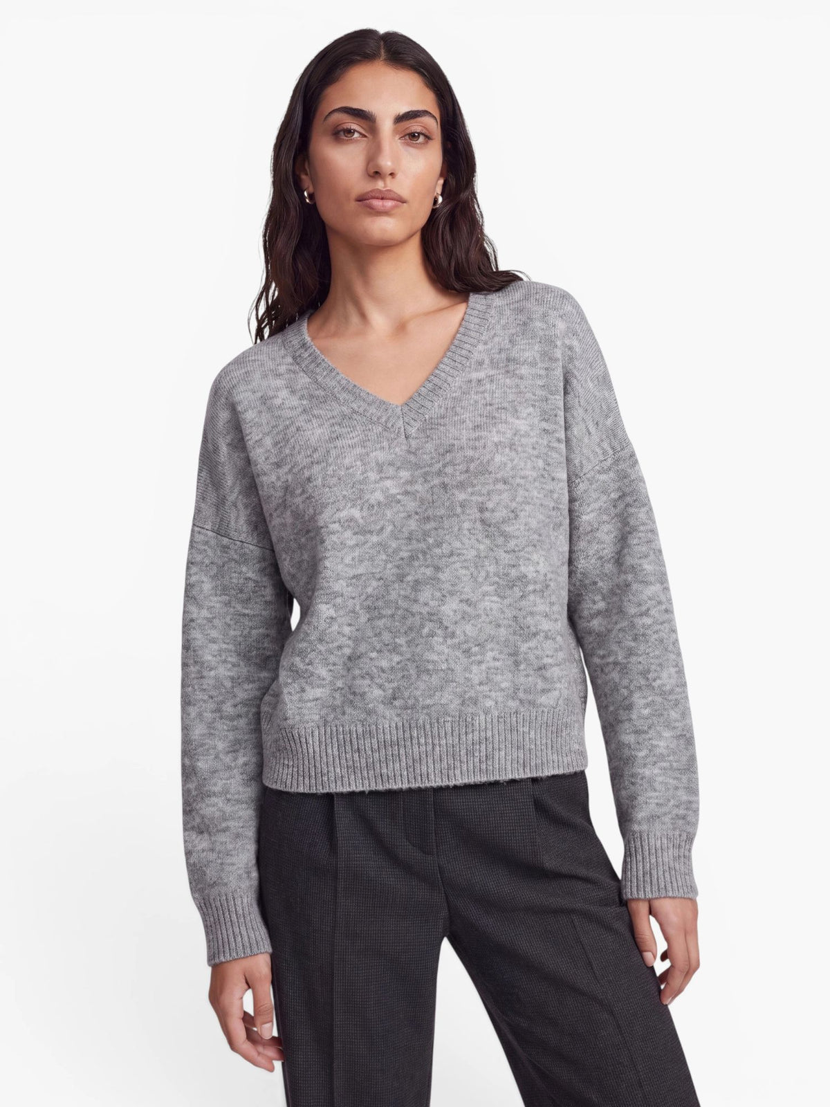 Eine Person mit langen, dunklen Haaren trägt den übergroßen grauen Pullover „Halina“ von LeGer by Lena Gercke sowie eine dunkle Hose und steht vor einem schlichten weißen Hintergrund.