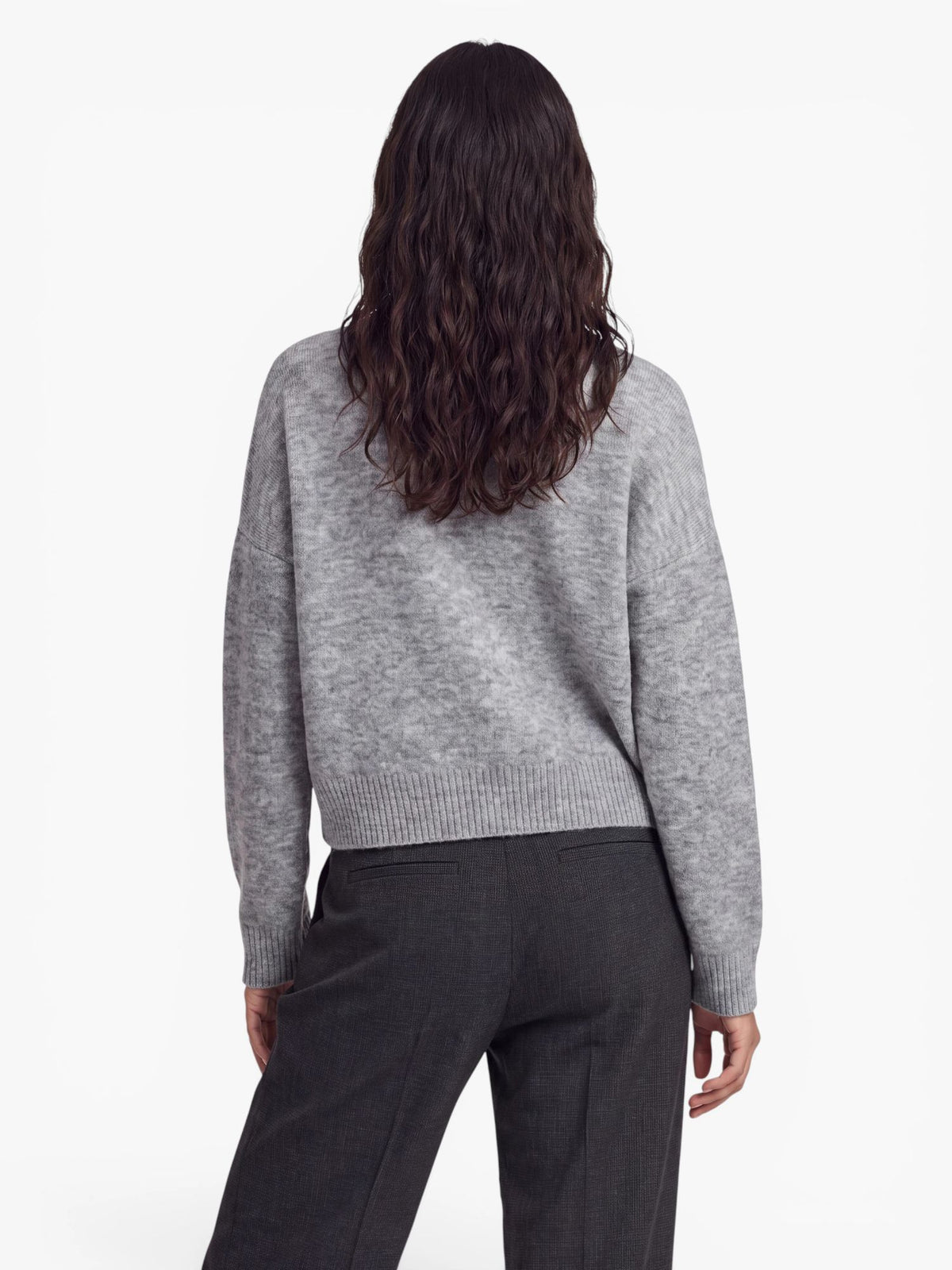 Eine Person mit langen, welligen braunen Haaren ist von hinten zu sehen. Sie trägt den übergroßen hellgrauen „Halina“-Pullover von LeGer by Lena Gercke mit dezentem V-Ausschnitt, dazu eine dunkelgraue Hose, und steht vor einem schlichten weißen Hintergrund.