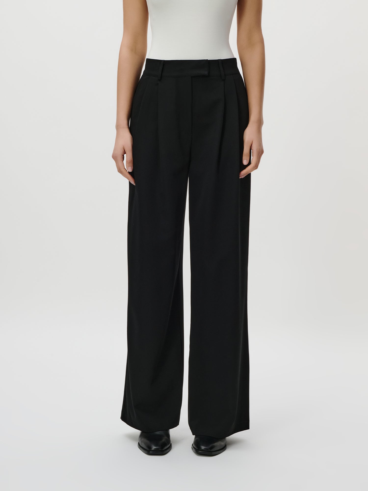 Eine Person in Größe 36 trägt die LeGer by Lena Gercke Annelie Pants Tall - eine schwarze, hochtaillierte Hose mit weitem Bein - mit einem weißen ärmellosen Oberteil vor einem einfarbig weißen Hintergrund. Nur der Körper von den Schultern abwärts ist sichtbar.