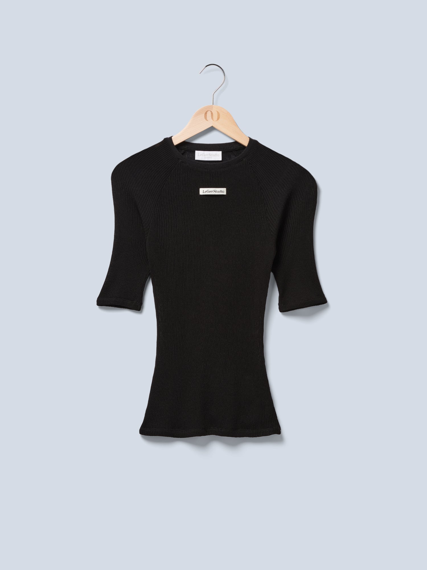 Das Abby T-Shirt von LeGer by Lena Gercke, ein schwarzes kurzärmliges Slim-Fit-Shirt aus Rippenstrick, hängt stilvoll auf einem Holzbügel vor einem hellgrauen Hintergrund und hat ein kleines weißes Etikett in der Nähe des Halsausschnitts.