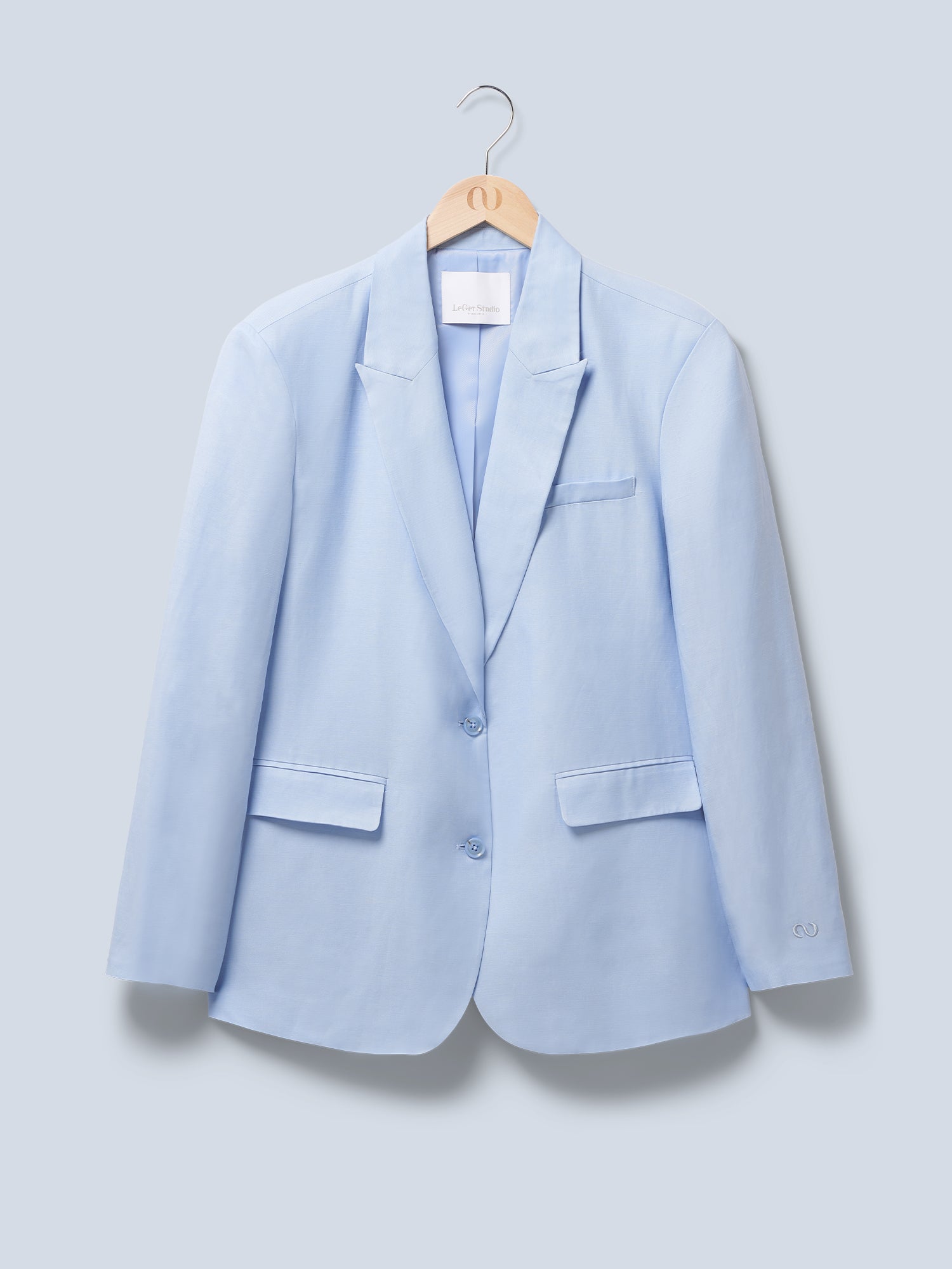 Der hellblaue „Majella“-Blazer von LeGer by Lena Gercke mit langen Ärmeln, zwei Knöpfen, einem Notch-Revers und drei Vordertaschen hängt auf einem Holzkleiderbügel vor einem hellen Hintergrund.