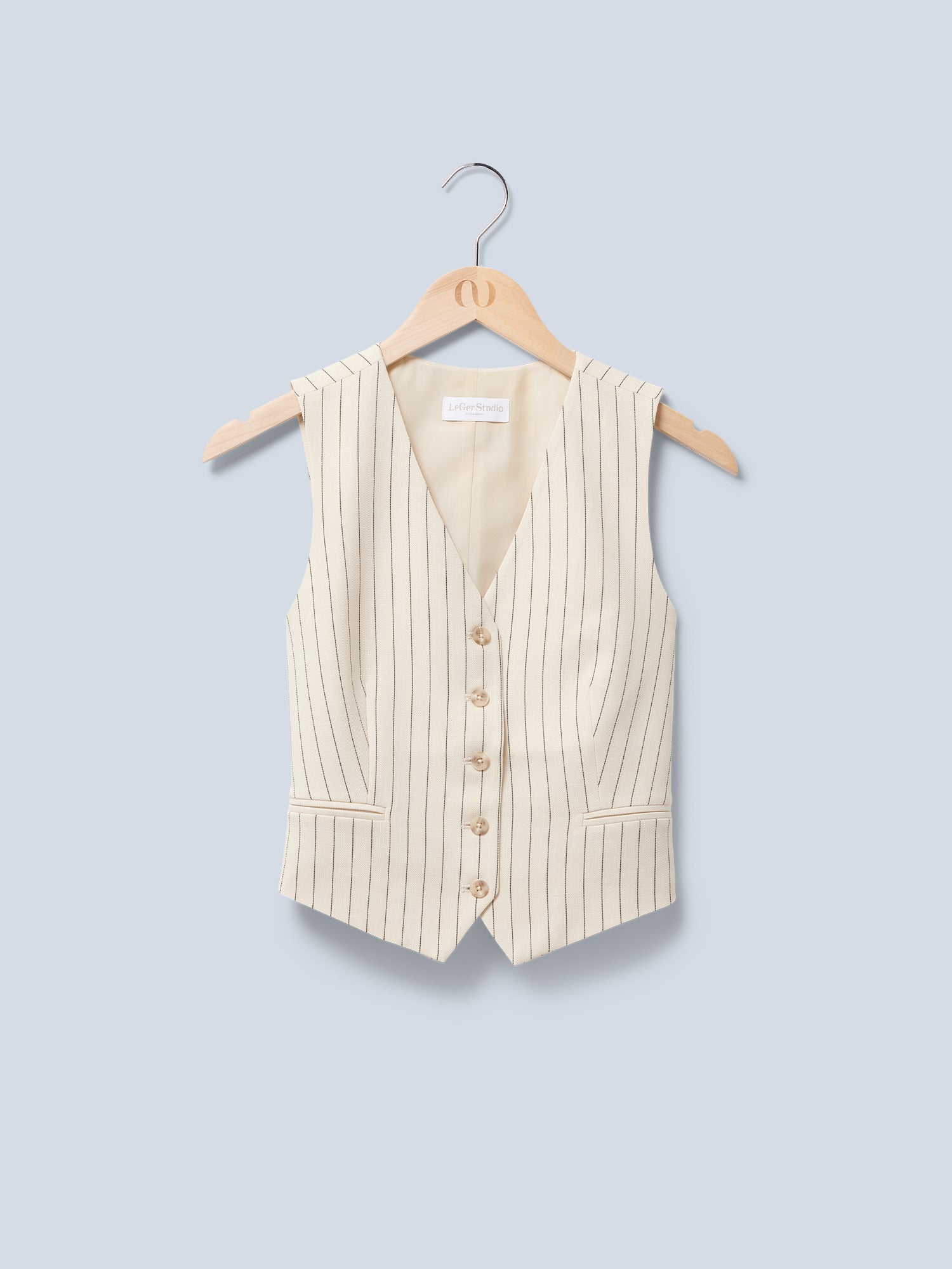 Die Elaine Vest von LeGer by Lena Gercke, eine beige ärmellose Weste mit Nadelstreifen und V-Ausschnitt, sechs Knöpfen und zwei Vordertaschen, hängt auf einem Holzbügel vor einem hellblauen Hintergrund.