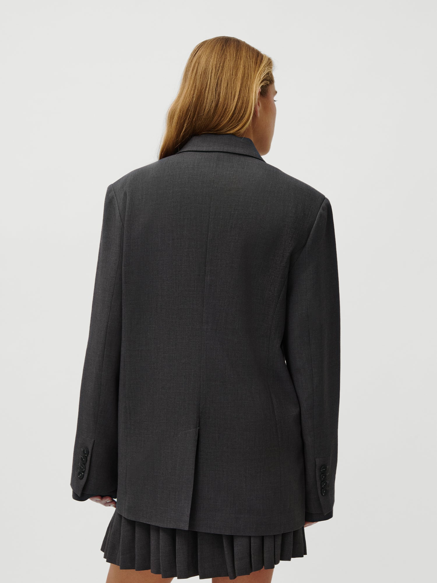 Eine Person mit langem, hellbraunem Haar ist von hinten zu sehen. Sie trägt den LeGer by Lena Gercke Franja Blazer aus der LeGer x Oh April Kollektion in lockerer Passform mit langen Ärmeln vor einem schlichten weißen Hintergrund.