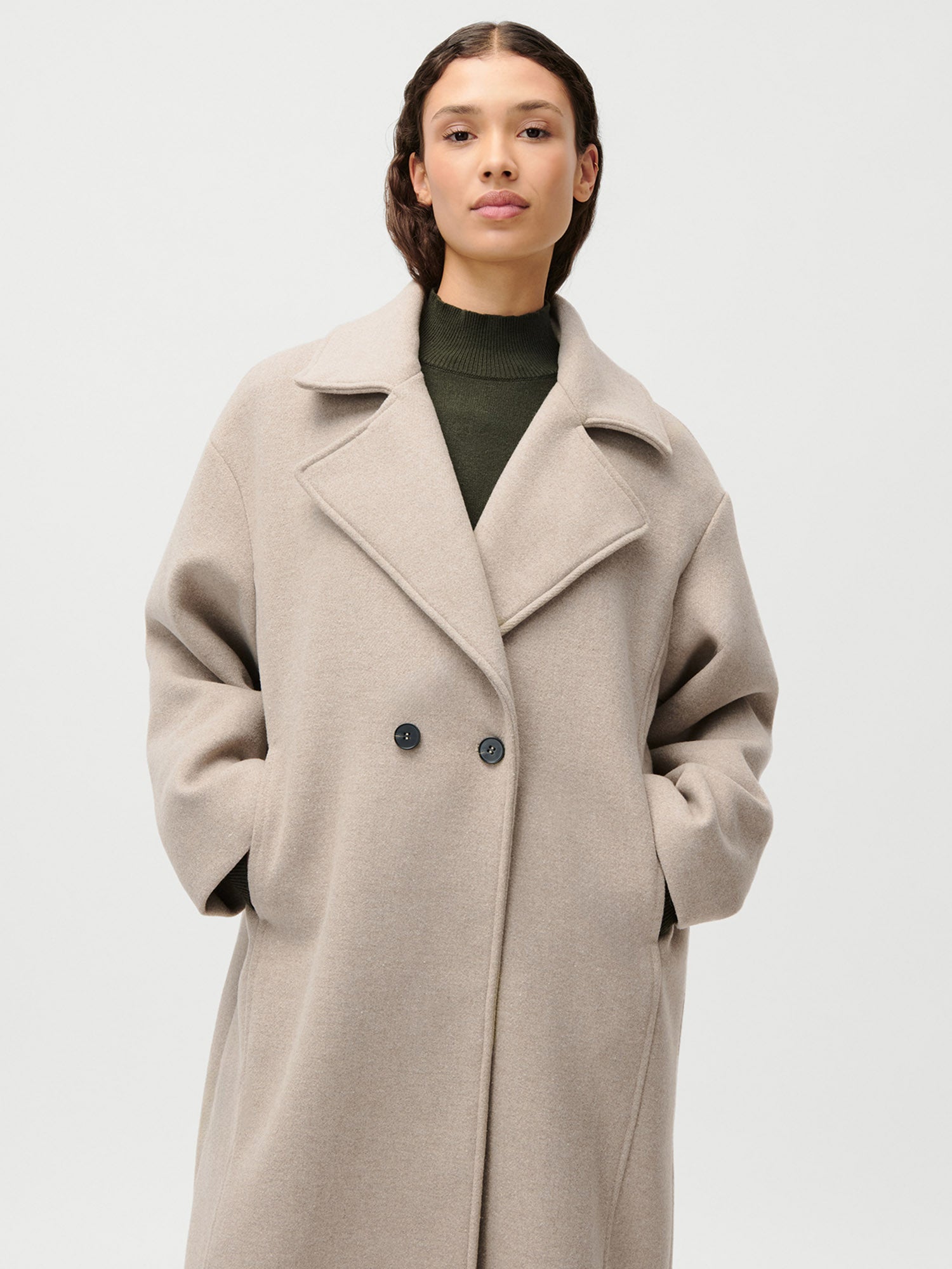 Eine Frau trägt den LeGer by Lena Gercke Nelly Coat in Größe 36 mit schwarzen Knöpfen und breitem Revers, die Hände in den Taschen über einem dunkelgrünen, hochgeschlossenen Oberteil, vor einem schlichten weißen Hintergrund.