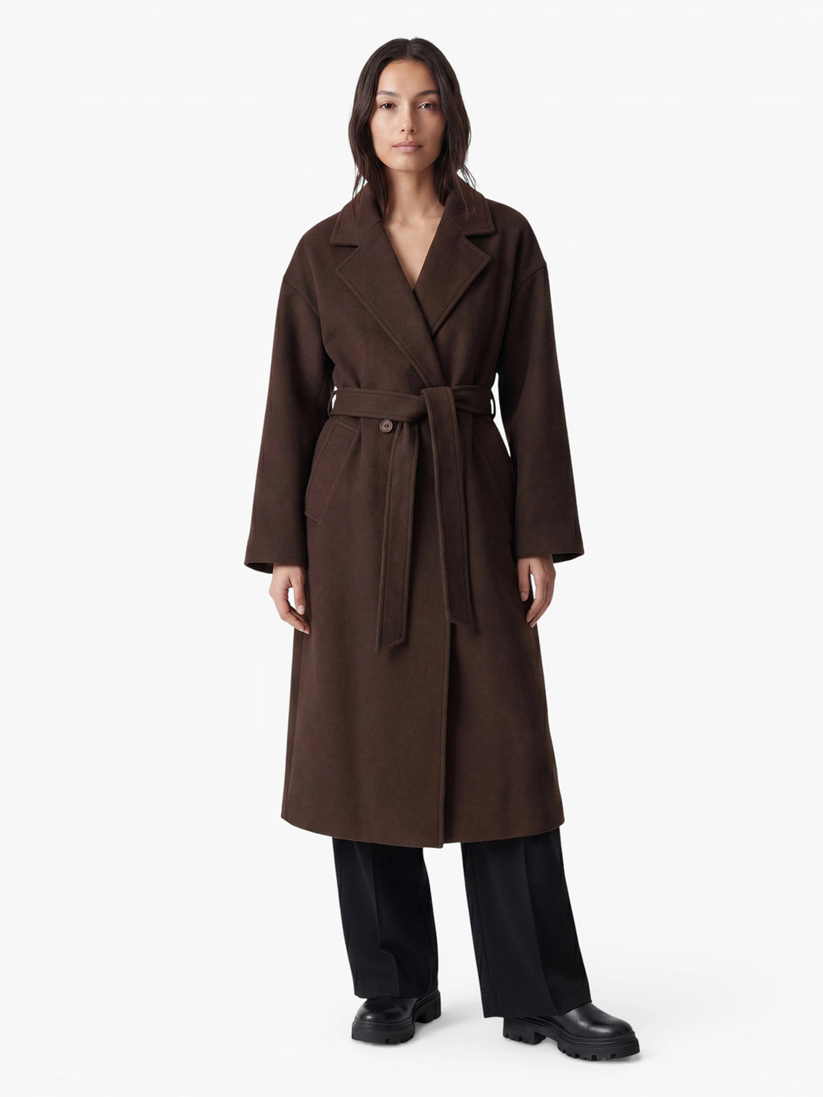 Eine Person, die einen dunkelbraunen „Betty“-Mantel von LeGer by Lena Gercke mit einem Gürtel in der Taille trägt, dazu eine schwarze Hose und schwarze Stiefel.