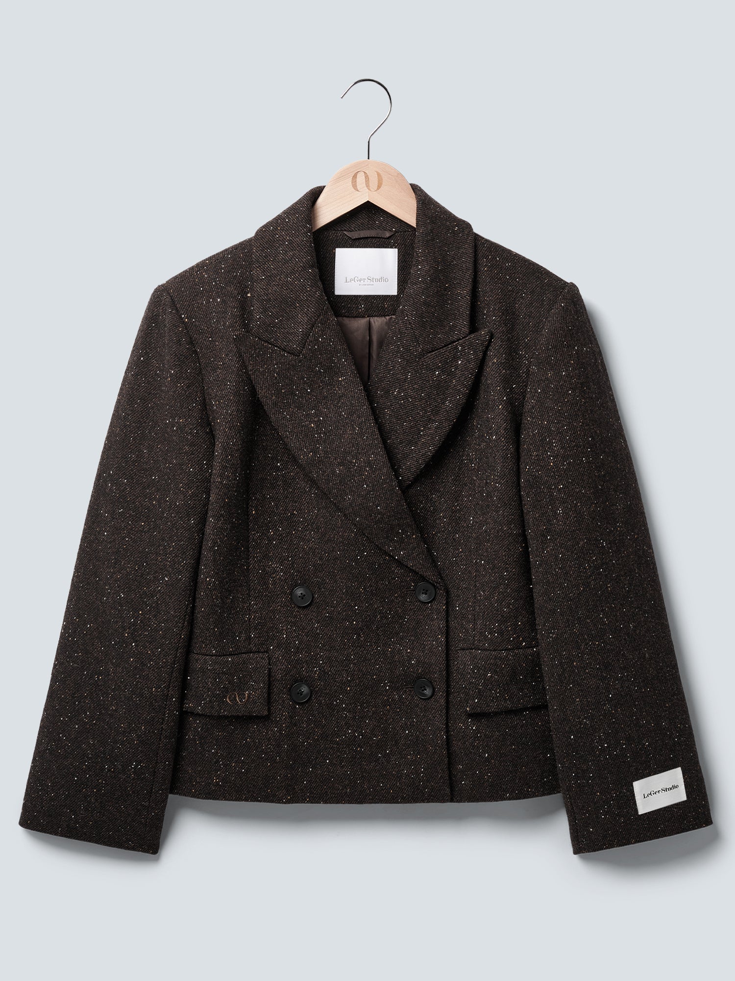 Der Libby Blazer von LeGer by Lena Gercke aus dunkler Wolle mit lockerer Passform, Doppelreiher-Design und speckelter Textur hängt an einem Holzkleiderbügel vor grauem Hintergrund. Weite Revers, Fronttaschen und weißes Label am linken Ärmel.