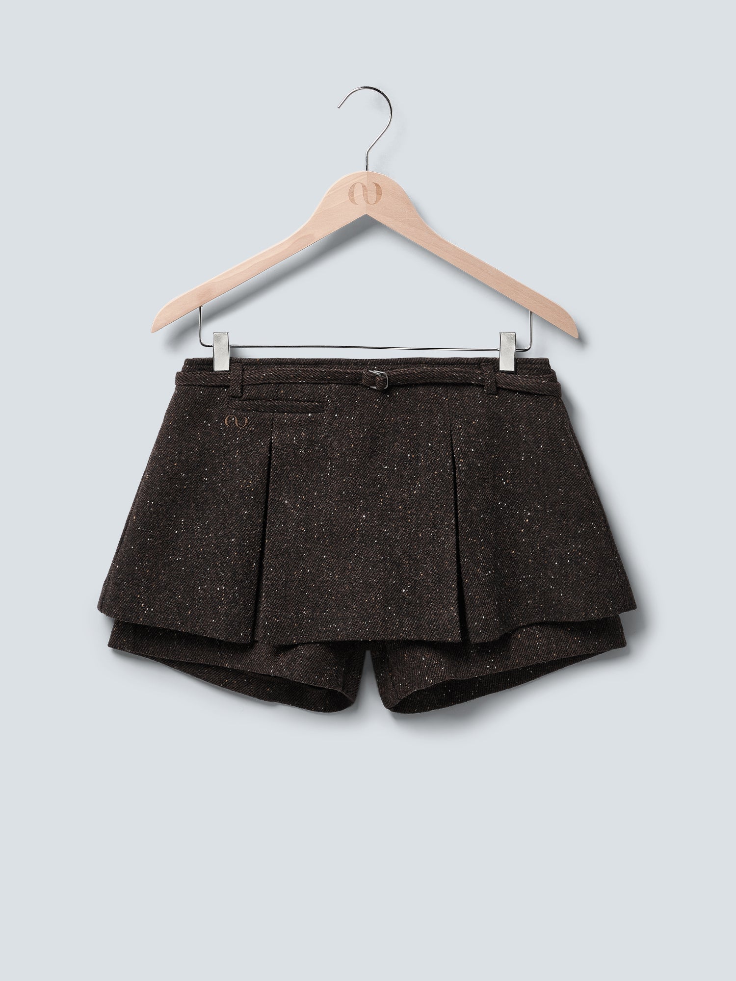 Der dunkelbraune, hoch taillierte Libby Skort von LeGer by Lena Gercke hat ein gesprenkeltes Muster, eine plissierte Vorderseite und einen schmalen Gürtel. Er wird in Minilänge auf einem Holzbügel vor einem hellgrauen Hintergrund gezeigt.