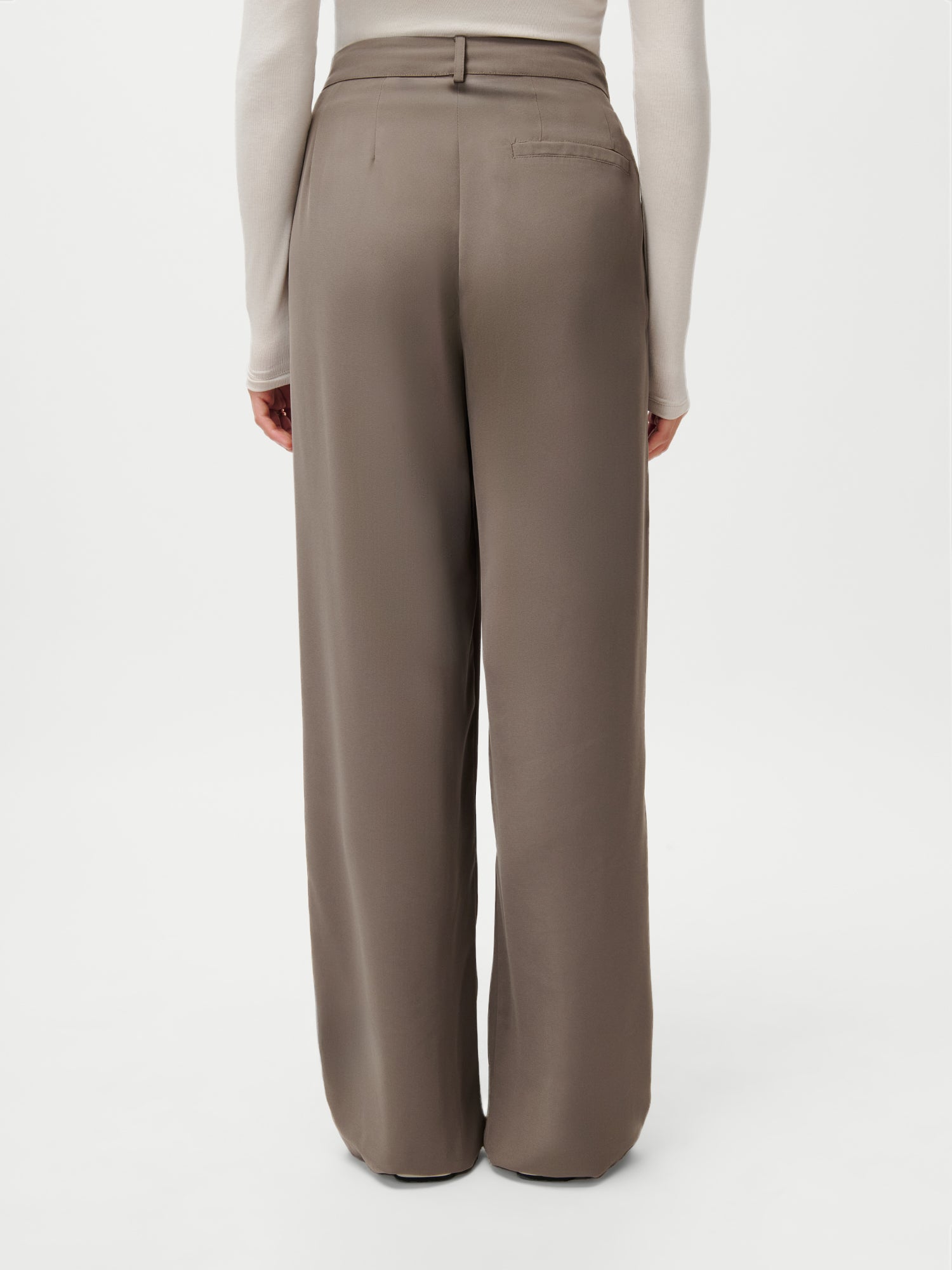 Eine von hinten gezeigte Person trägt die LeGer x Purelei - Cara Pants by LeGer by Lena Gercke in Taupe mit hoher Taille und weitem Bein (Größe 36) mit einem taillierten beigefarbenen langärmeligen Oberteil. Modelgröße: 1,72 m; fotografiert vor einem schlichten weißen Hintergrund.
