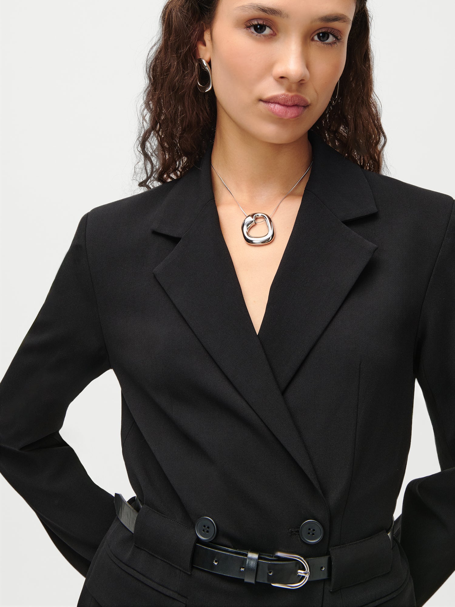 Eine Frau trägt das schwarze LeGer x Purelei „Jolina“-Kleid von LeGer by Lena Gercke, dazu eine runde silberne Halskette und Creolen, und steht selbstbewusst da, eine Hand auf die Hüfte gestützt.