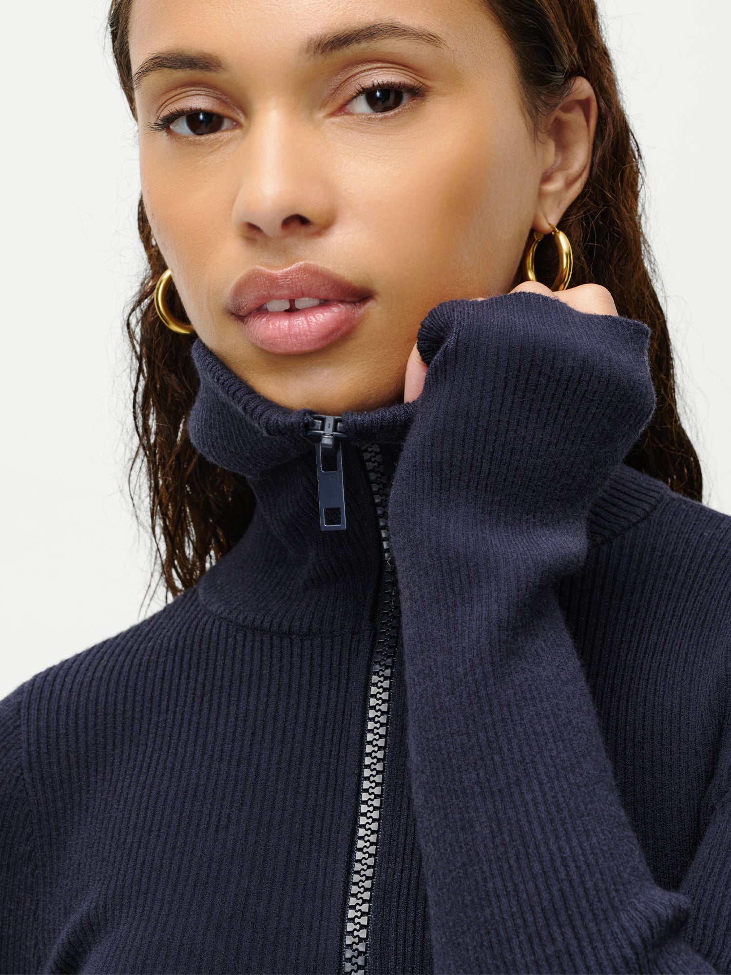 Eine Frau mit langen braunen Haaren und goldenen Ohrringen trägt den LeGer by Lena Gercke Heidi Body und hält das Halsband dicht an ihr Gesicht, während sie mit neutraler Miene in die Kamera schaut.