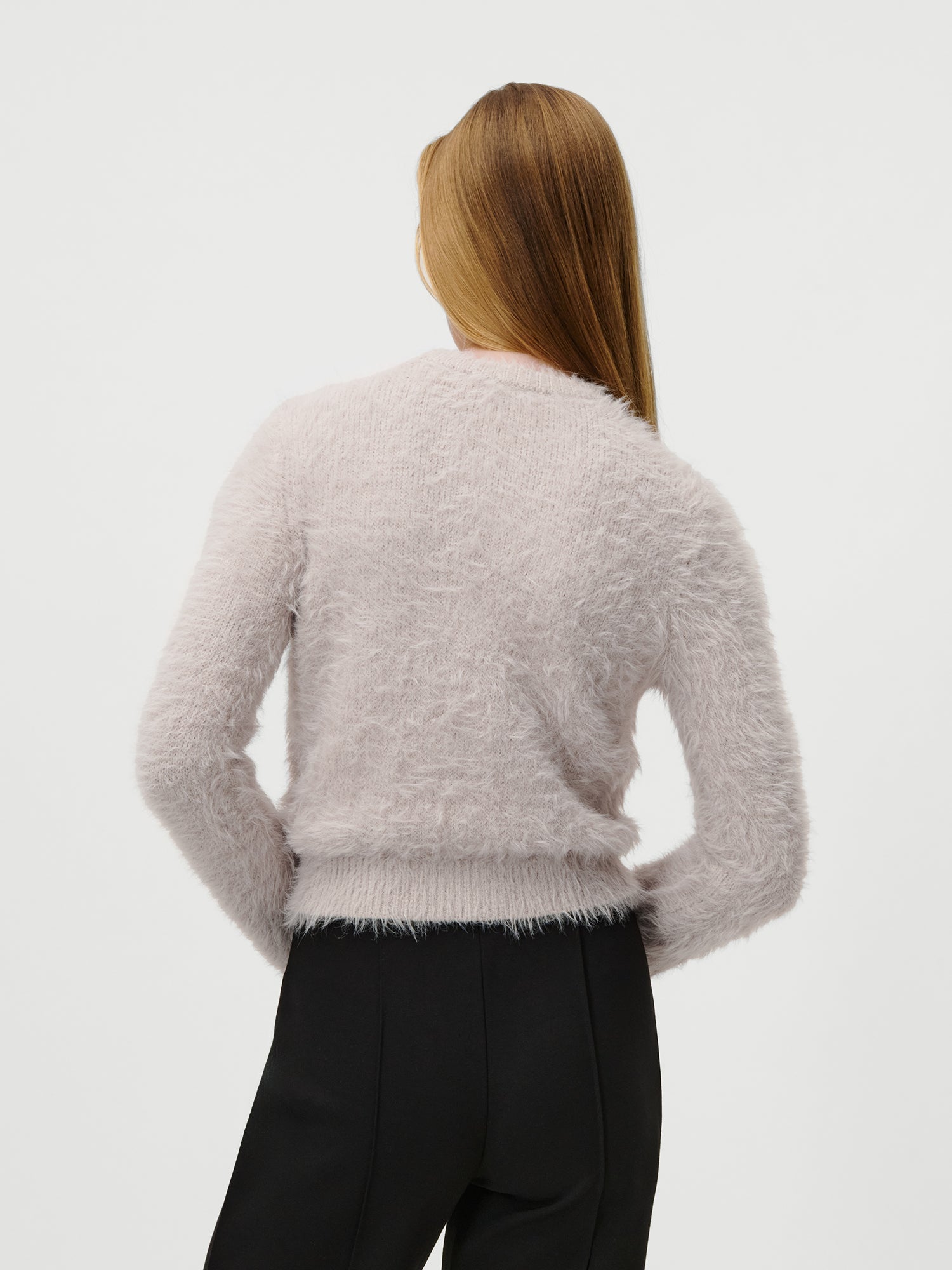 Eine Person mit langem, glattem, hellbraunem Haar wird von hinten gezeigt. Sie trägt den LeGer by Lena Gercke Sharon Jumper in Größe 36 - einen flauschigen, hellrosa Langarmpullover - und eine schwarze Hose vor einem schlichten weißen Hintergrund.