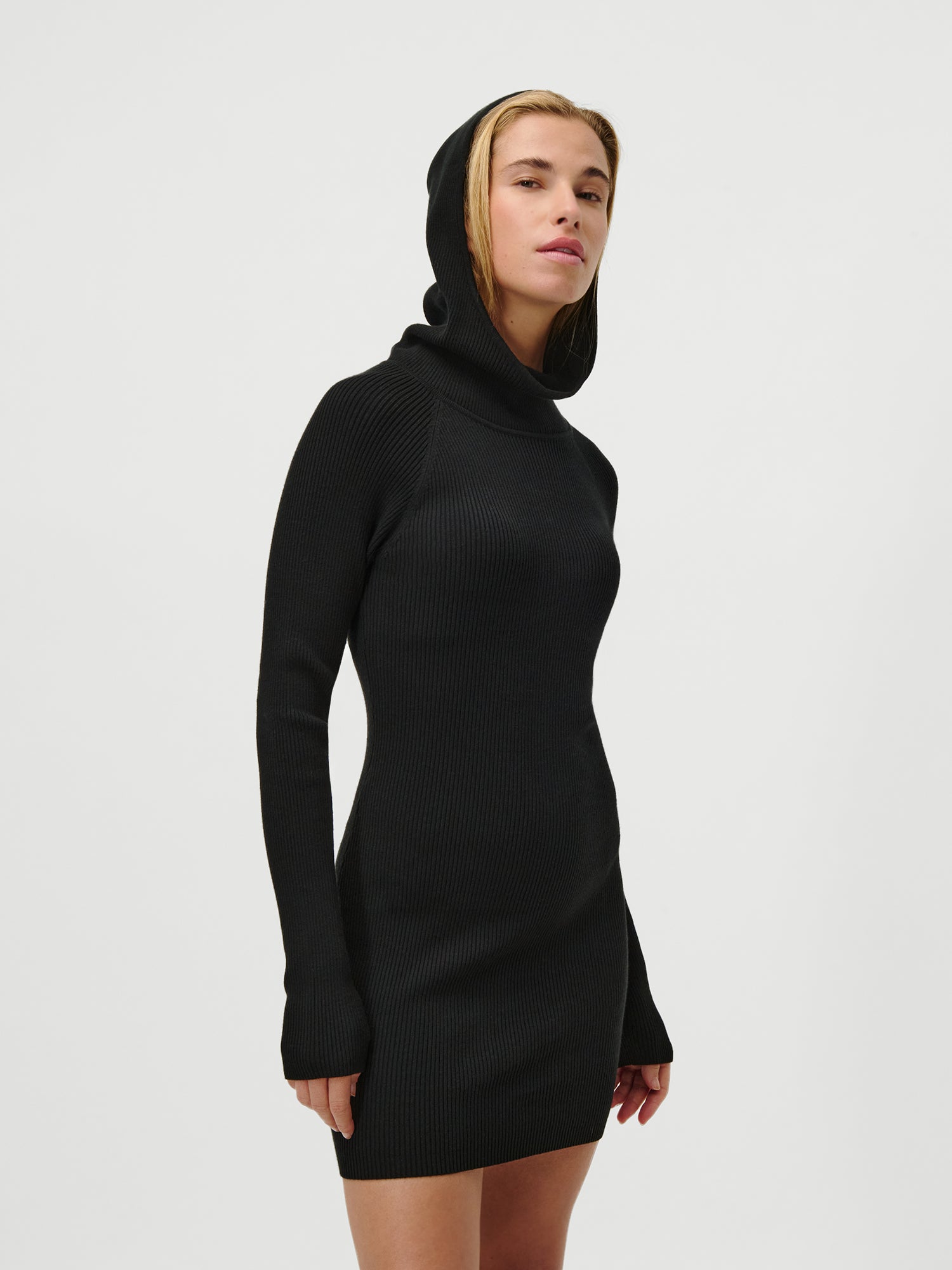 Eine Person in dem Mathilde Dress von LeGer by Lena Gercke, einem schmal geschnittenen, langärmeligen Minikleid mit Kapuze, steht selbstbewusst vor einem weißen Hintergrund und schaut in die Kamera.