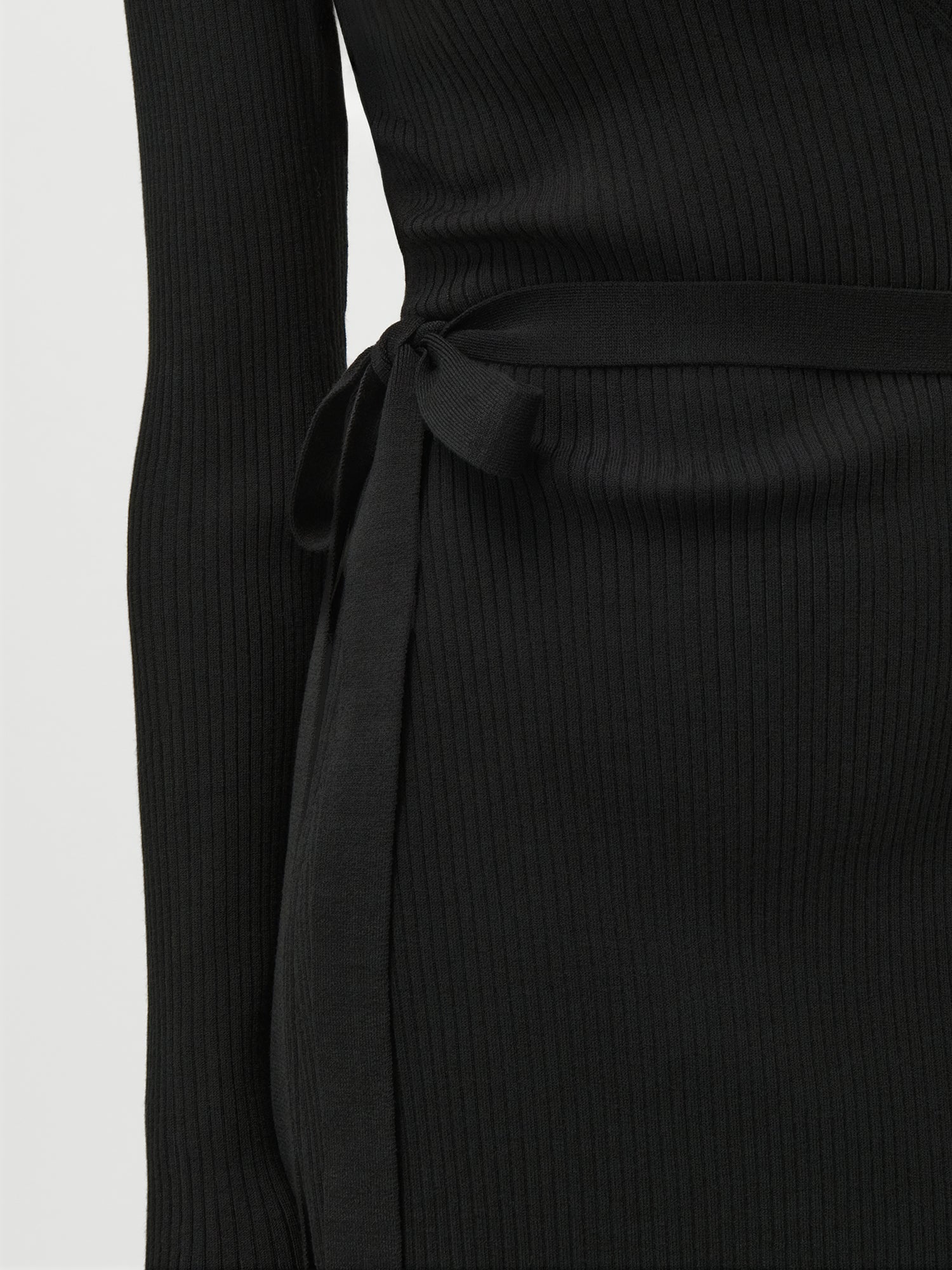 Nahaufnahme einer Person, die das Effie Dress von LeGer by Lena Gercke trägt - ein figurbetontes, schwarzes langärmeliges Rippenkleid mit einem passenden Stoffgürtel in der Taille. Der Hintergrund ist einfarbig und hell.