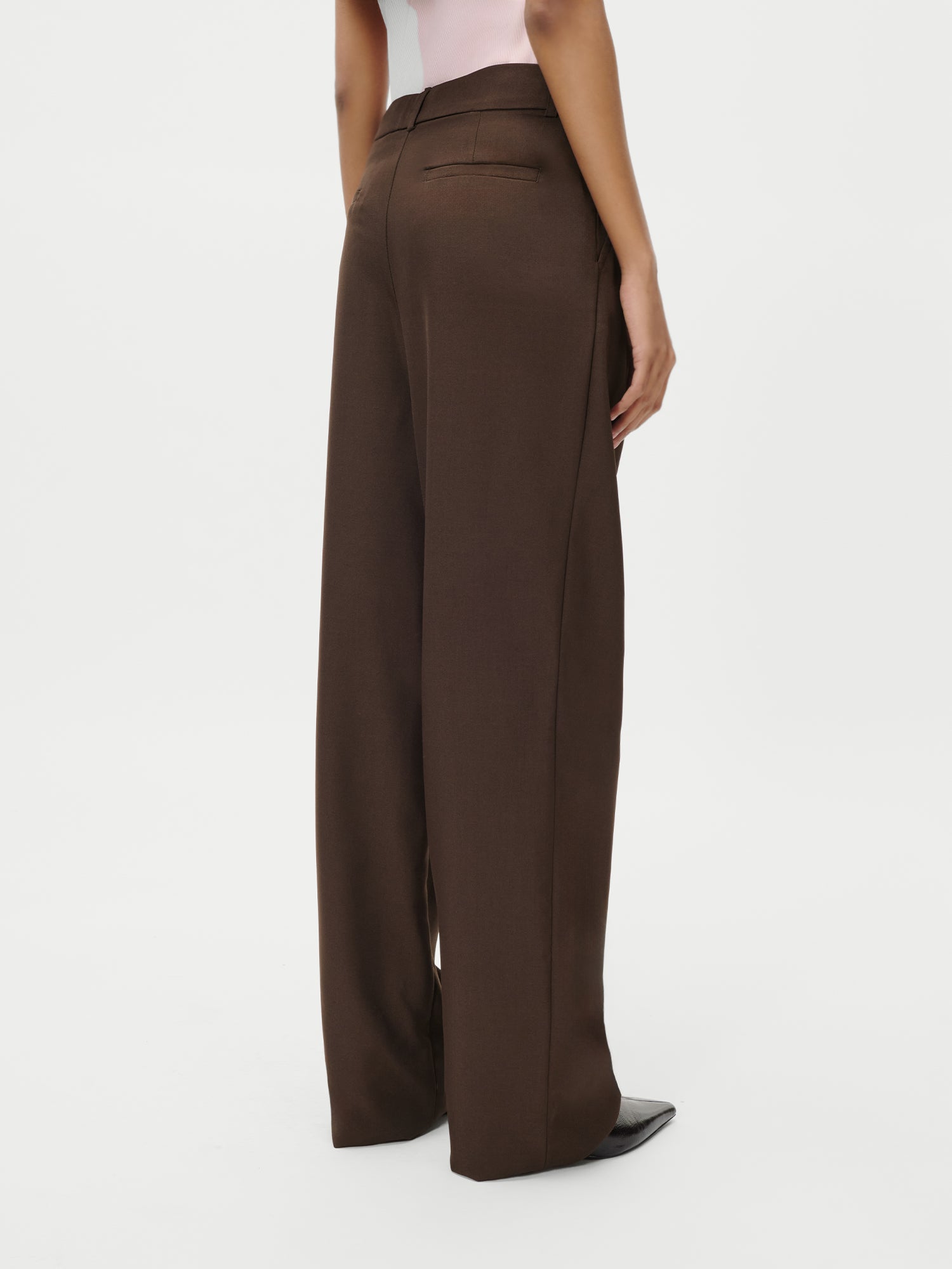 Eine Person modelliert die Jerika Pants von LeGer by Lena Gercke - eine braune Hose mit hoher Taille und weitem Bein und schwarzen spitzen Schuhen, von hinten vor weißem Hintergrund - ideal zu einem Maxikleid in Größe 36.