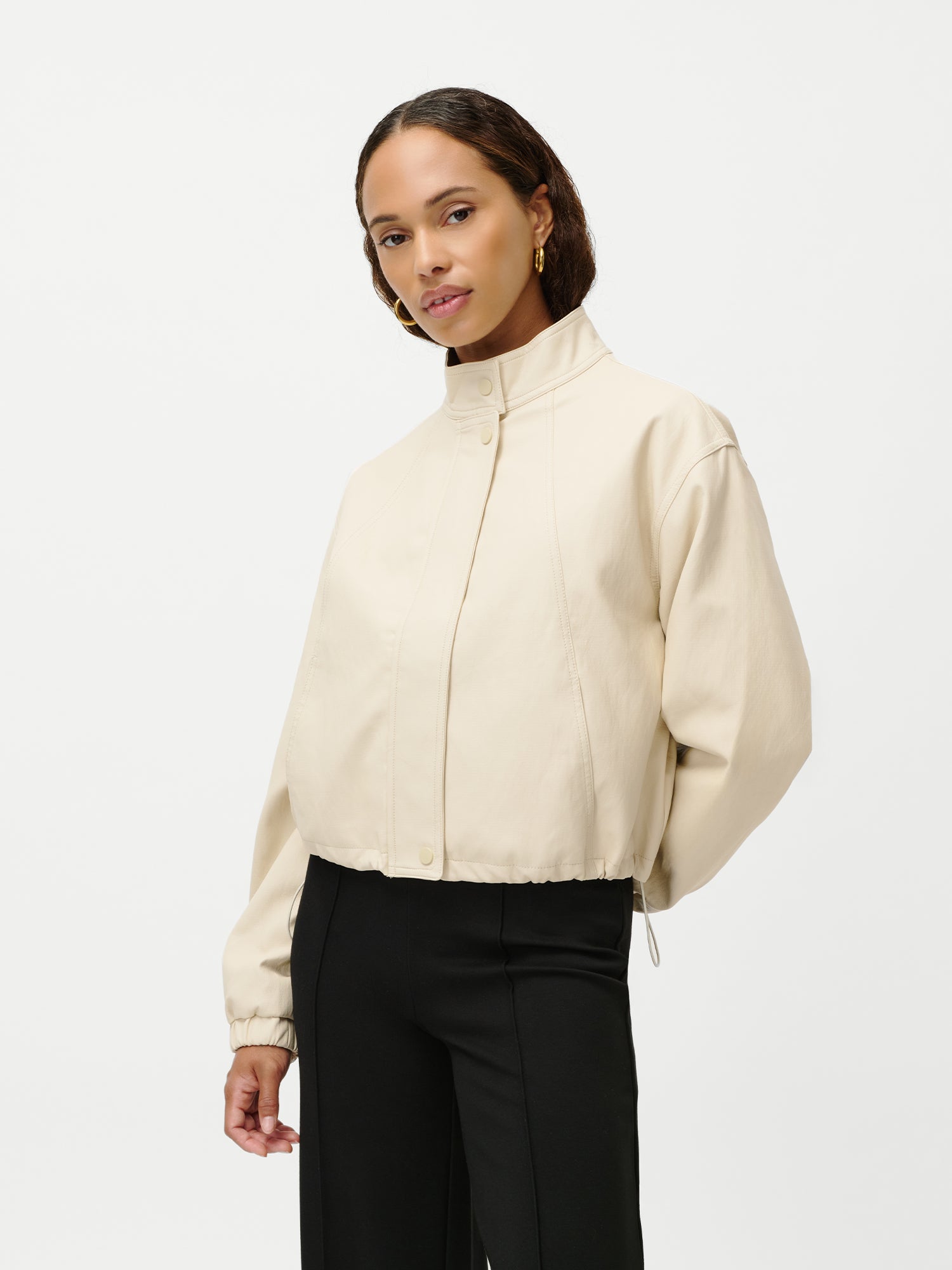 Eine Frau steht vor einem weißen Hintergrund und trägt die LeGer by Lena Gercke Janet Jacket in Hellbeige, Größe 36, mit verkürzter Passform und langen Ärmeln, gepaart mit einer schwarzen Hose. Sie hat ihr Haar zurückgesteckt und trägt dazu goldene Ohrringe.