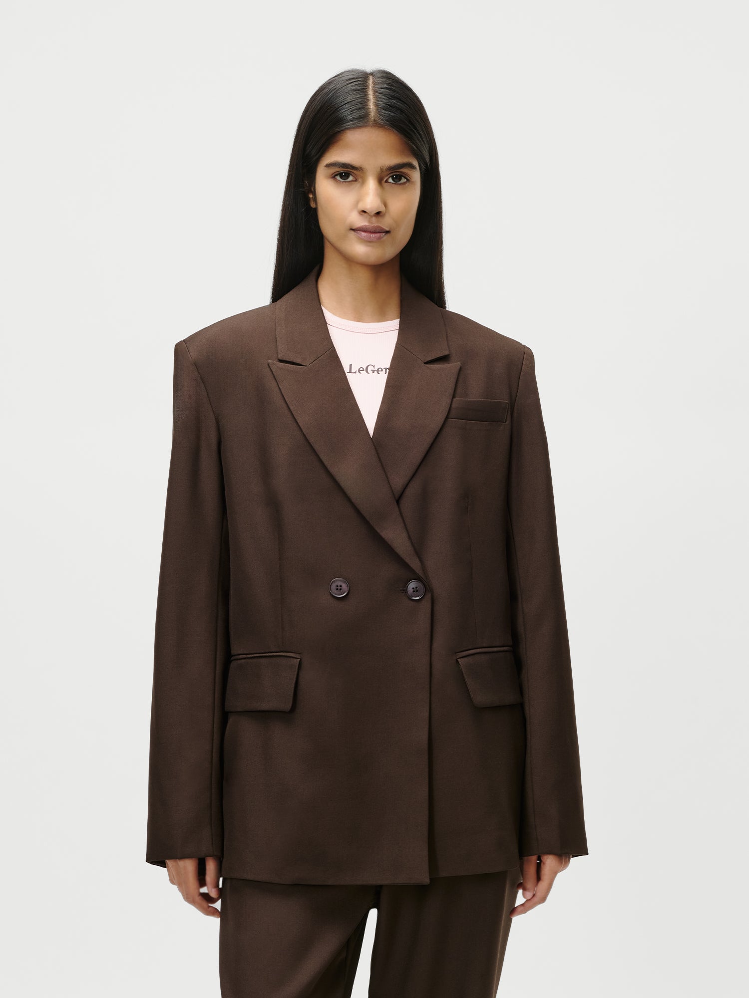 Eine Person mit langen, glatten dunklen Haaren trägt einen locker sitzenden braunen Jerika Blazer von LeGer by Lena Gercke in Größe 36 über einem blassrosa Oberteil vor einem schlichten weißen Hintergrund.