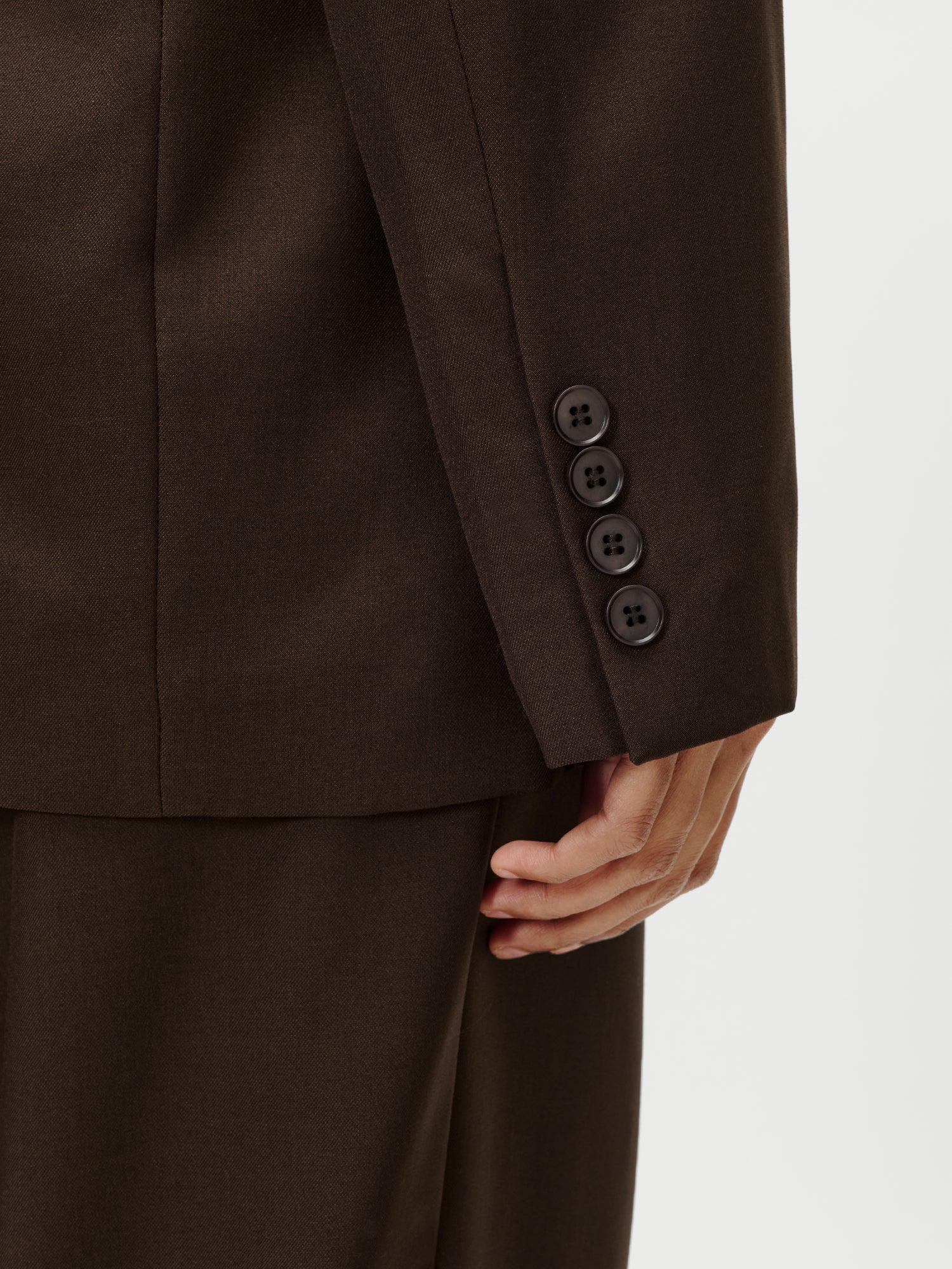 Nahaufnahme einer Person in einem dunkelbraunen Jerika-Blazer von LeGer by Lena Gercke, die den Ärmel mit vier Manschettenknöpfen und ihre Hand an der Seite zeigt; der Blazer hat die Größe 36 in normaler Länge.