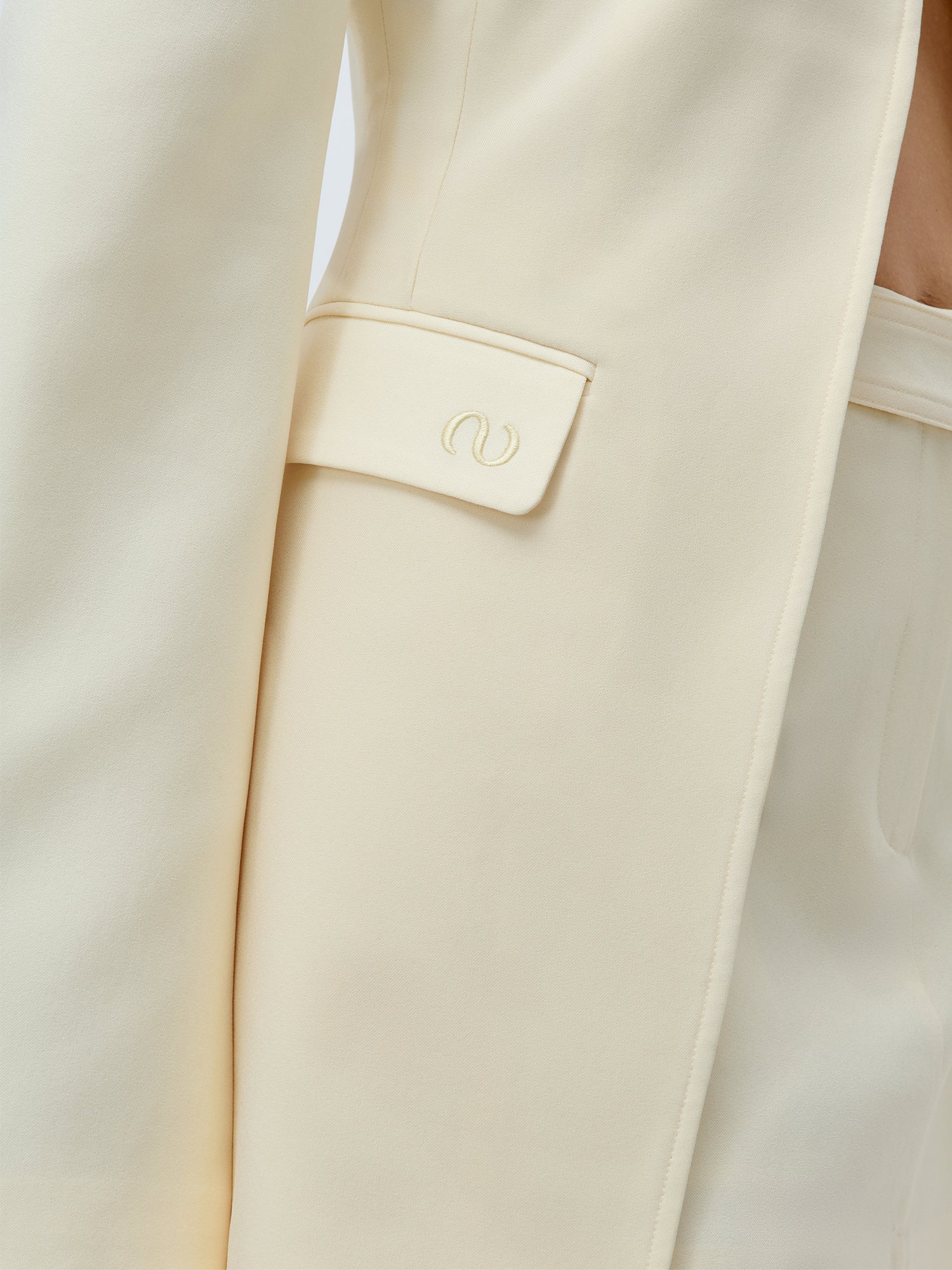 Nahaufnahme des Cim Blazers von LeGer by Lena Gercke in creme, mit regulärer Passform und strukturiertem Schulterpolster. Der Fokus liegt auf der Seitentasche mit einer Klappe mit gesticktem Schnörkel, die den glatten Stoff und die maßgeschneiderten Details hervorhebt.