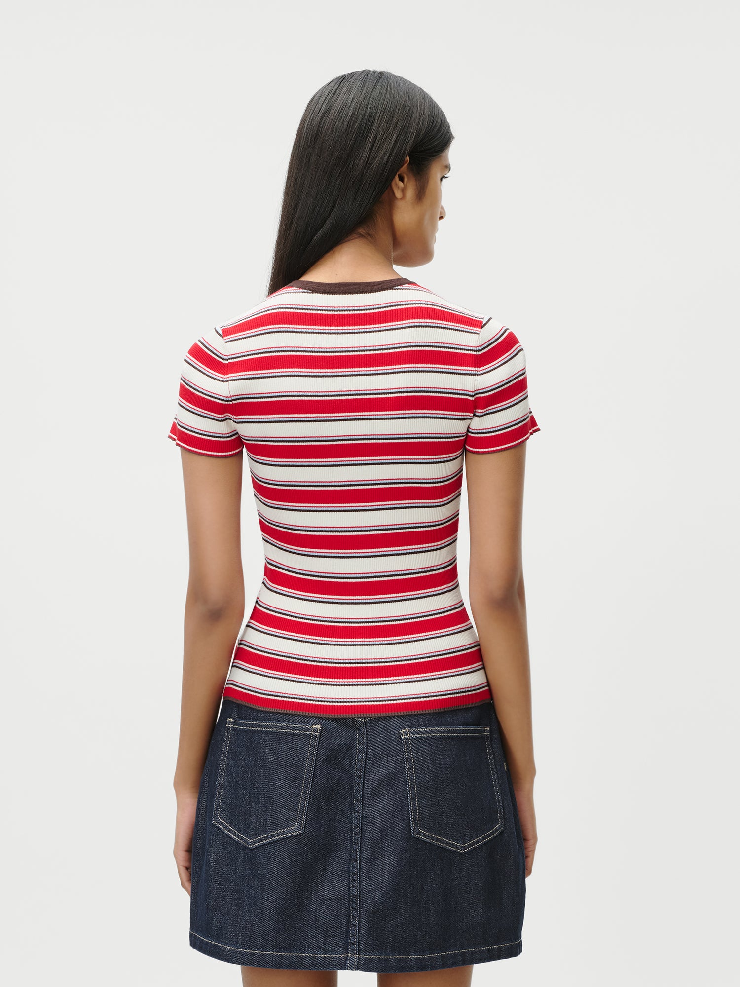 Eine Frau mit langen dunklen Haaren ist von hinten zu sehen. Sie trägt das Danielle T-Shirt von LeGer by Lena Gercke mit schmalen roten, weißen und rosa Streifen, gepaart mit einem dunkelblauen Jeansrock mit zwei Gesäßtaschen in Größe 36 vor weißem Hintergrund.