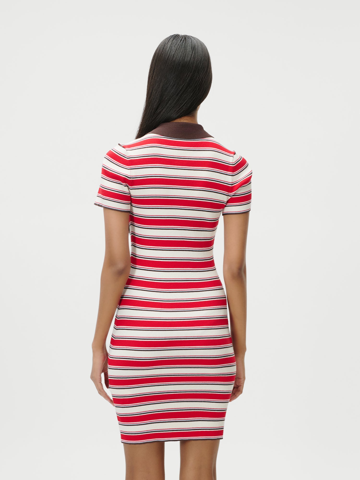 Eine Frau mit langen dunklen Haaren steht in dem Kleid Elenia von LeGer by Lena Gercke, einem knielangen, schmal geschnittenen Kleid mit roten, weißen und rosafarbenen Streifen und einem dunklen Kragen, vor einem schlichten weißen Hintergrund.