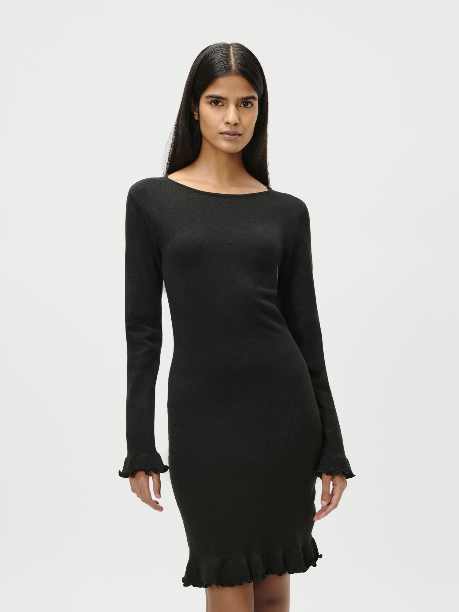 Eine Frau mit extra langem, glattem Haar trägt das LeGer by Lena Gercke Marlen Dress - ein schmal geschnittenes, schwarzes Minikleid mit langen Ärmeln und gerüschten Manschetten - vor einem schlichten weißen Hintergrund.