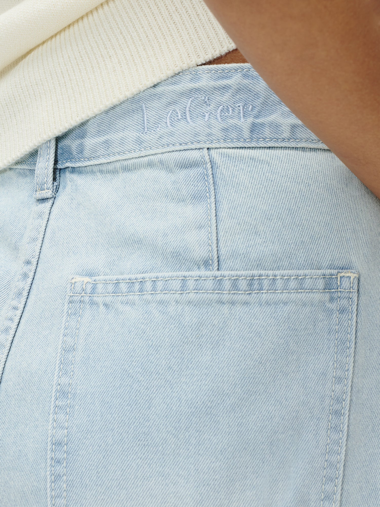 Nahaufnahme der Gesäßtasche der hellblauen Denim-Hose Eilika von LeGer by Lena Gercke mit der Stickerei "Le Ger" über der Tasche. Ein cremefarbenes Oberteil ist teilweise sichtbar - ideal mit Größe 36 lange Kleider oder Ihrem Lieblings-Maxikleid.