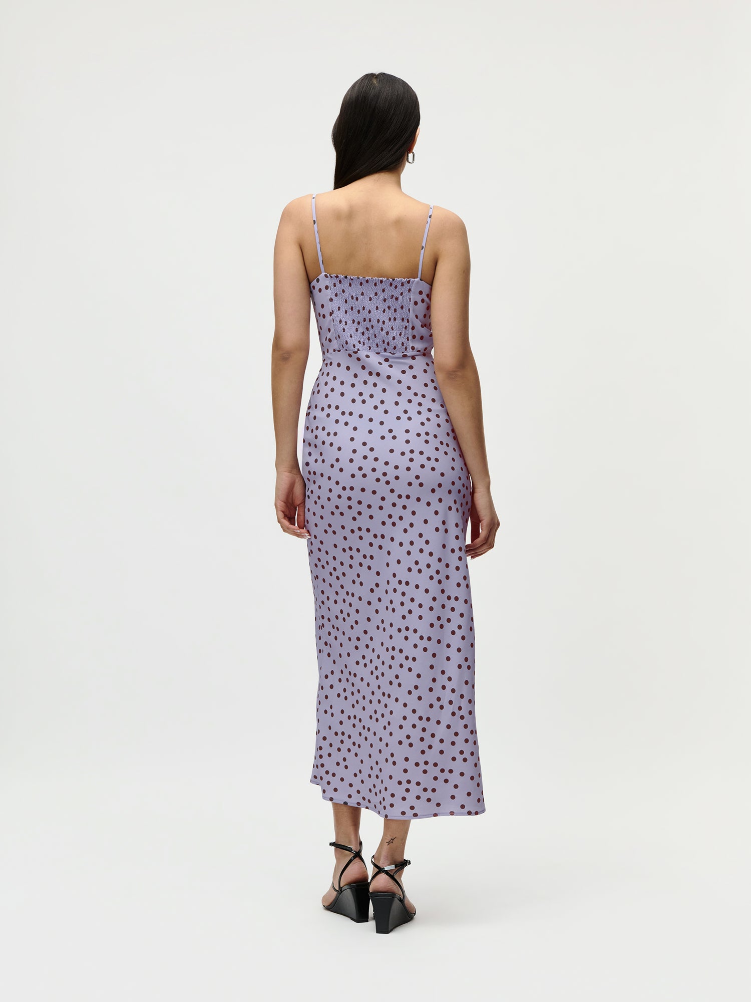 Eine Frau mit langen dunklen Haaren trägt das LeGer by Lena Gercke Fleur Dress - ein knöchellanges lilafarbenes Kleid mit dünnen Trägern und schwarzen Tupfen - auf schwarzen Riemchenabsätzen vor einem schlichten weißen Hintergrund für einen schicken Sommerlook.