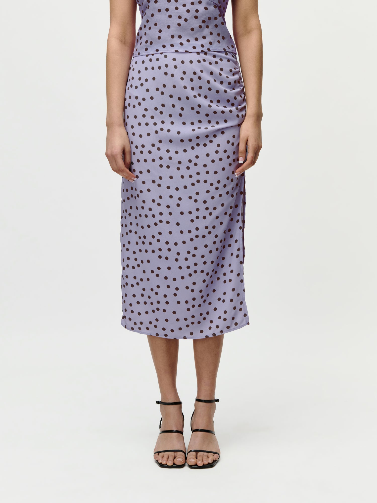 Eine Person trägt das Fleur Set von LeGer by Lena Gercke, ein hellviolettes ärmelloses Midikleid mit schwarzen Polka Dots in Größe 36 und schwarze Riemchensandalen. Set kaufen und genießen Sie einen Preisvorteil! Hintergrund: schlichtes Weiß.