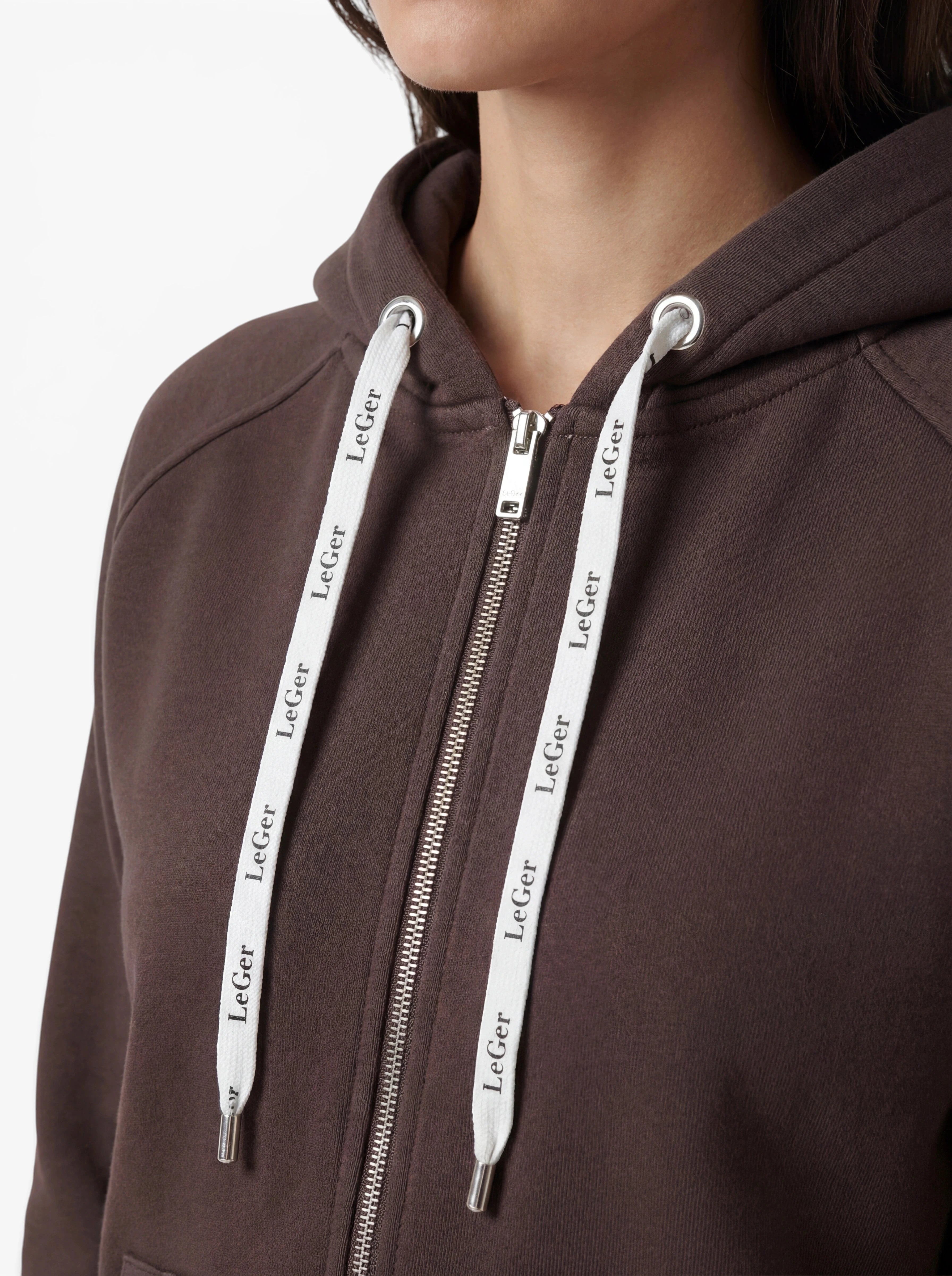 Nahaufnahme einer Person, die den „Phoenix“-Hoodie von LeGer by Lena Gercke trägt – ein brauner Hoodie mit Reißverschluss und weißen Kordeln, auf denen der Markenname zu sehen ist. Zu sehen sind nur der untere Teil des Gesichts und die Brust, wodurch der sportliche Schnitt und das strapazierfähige Design besonders gut zur Geltung kommen.