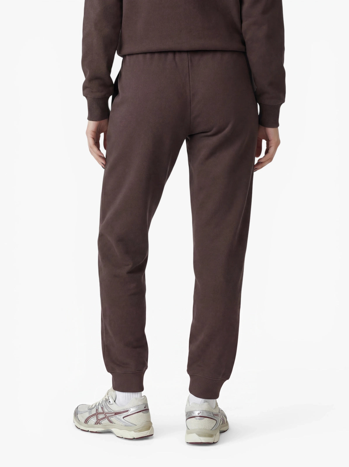 Eine Person, die eine braune Jogginghose im „Nela“-Stil von LeGer by Lena Gercke aus Stretchstoff sowie weiße Sneaker trägt, ist von hinten vor einem schlichten weißen Hintergrund zu sehen. Die taillierte Passform unterstreicht die moderne und bequeme Silhouette.