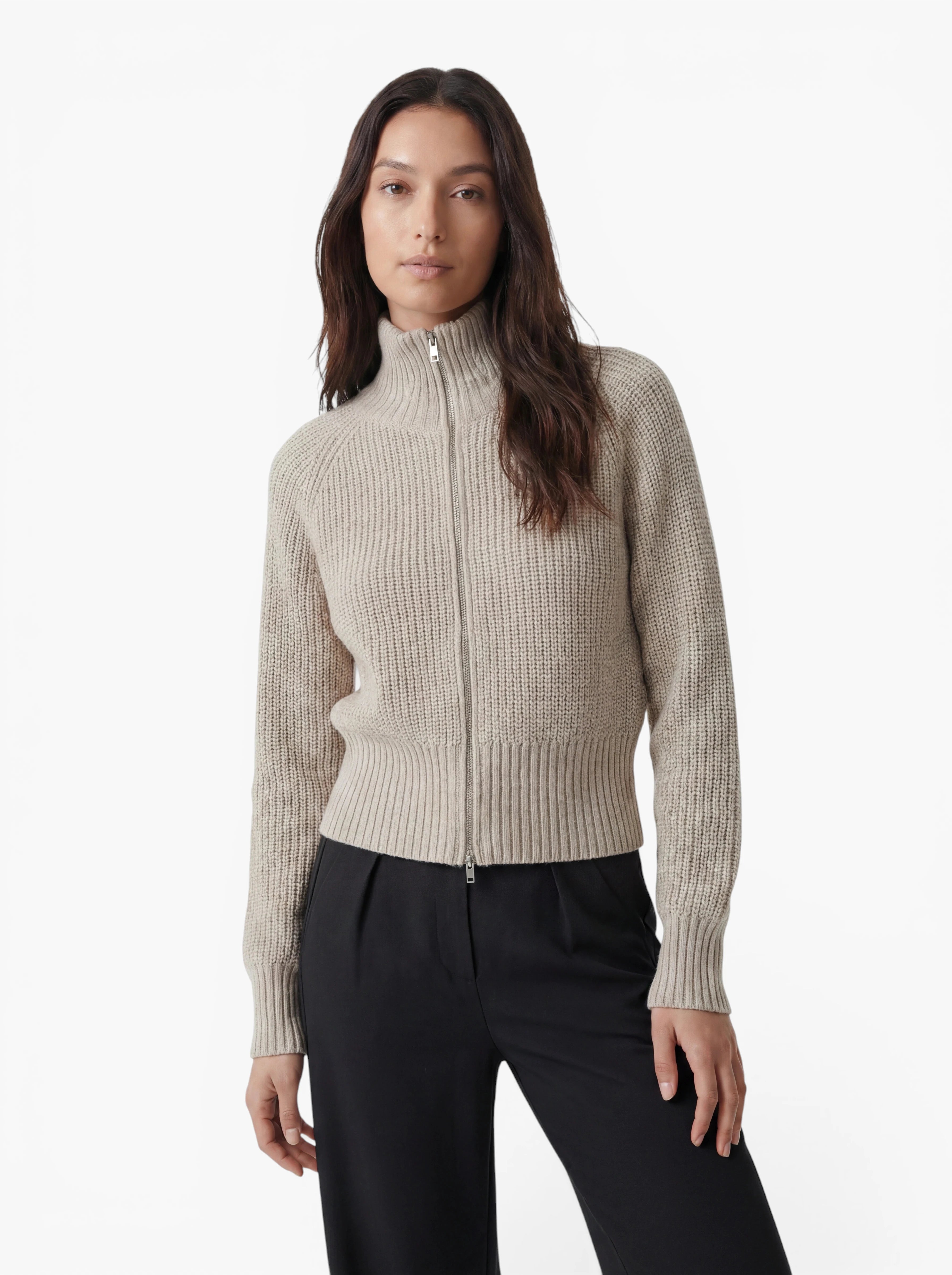 Eine Person, die den Pullover „Nala“ von LeGer by Lena Gercke trägt – einen eleganten, beigen Strickpullover mit Reißverschluss und hohem Kragen –, steht in Kombination mit einer schwarzen Hose vor einem schlichten weißen Hintergrund.