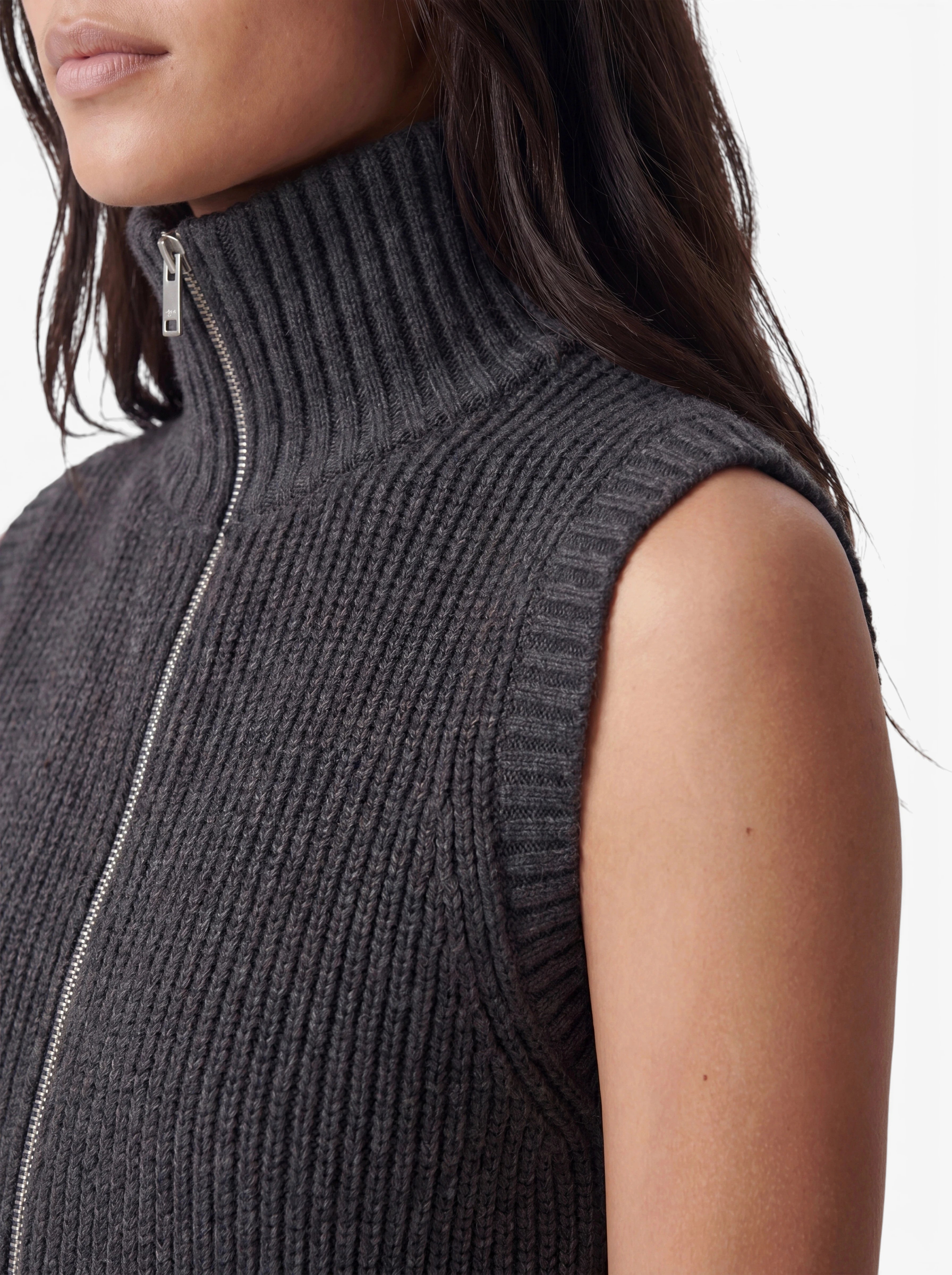 Eine Frau trägt die ärmellose, gerippte Rollkragenweste „Betsy“ mit Reißverschluss von LeGer by Lena Gercke, die sich durch ein minimalistisches Design in Dunkelgrau auszeichnet. Die Weste wird vor einem weißen Hintergrund von den Schultern aufwärts gezeigt.