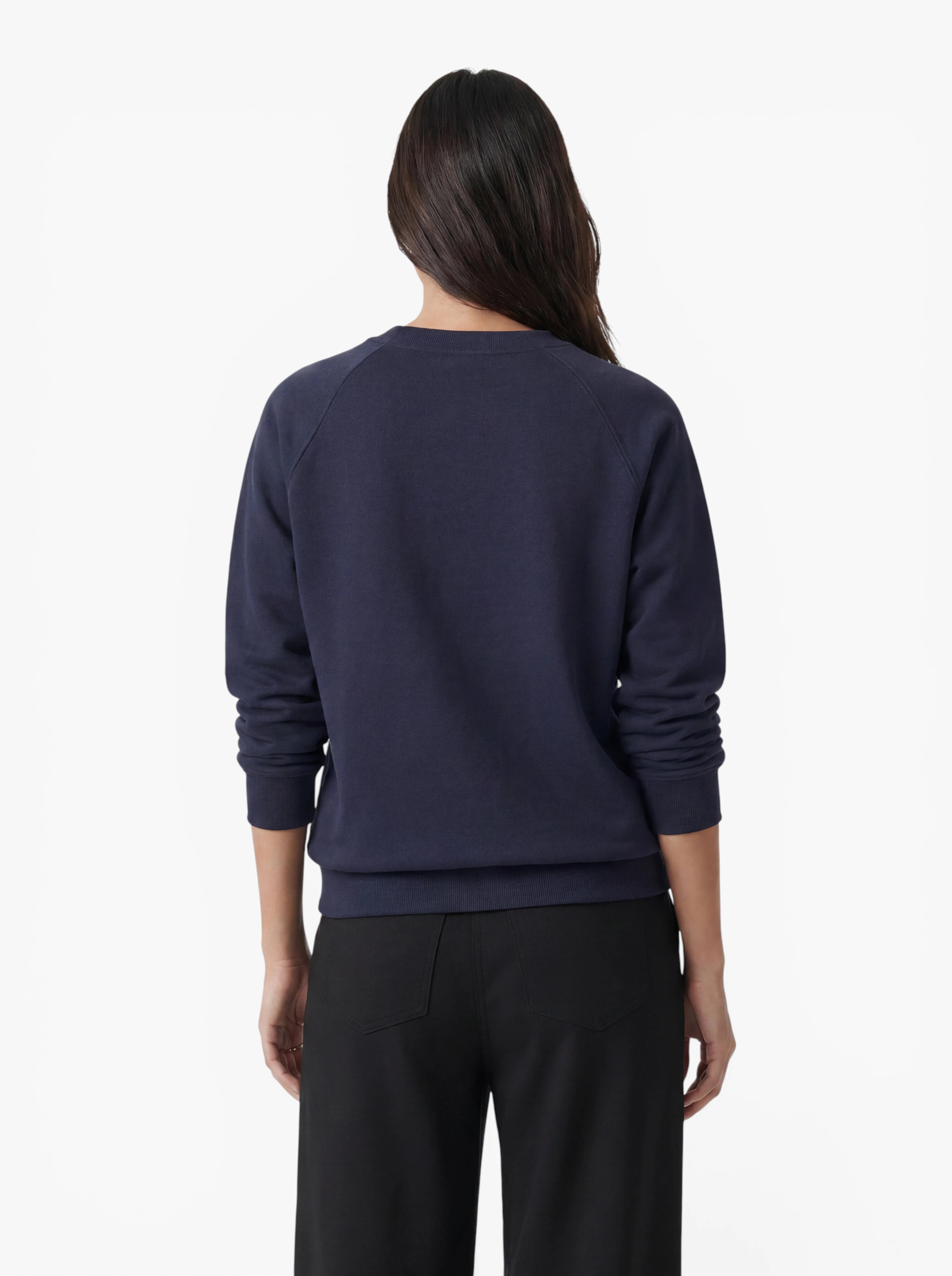 Vor einem schlichten weißen Hintergrund steht eine Person mit langen dunklen Haaren mit dem Rücken zur Kamera. Sie trägt den marineblauen „Bettina“-Pullover von LeGer by Lena Gercke in lockerer Passform sowie eine schwarze Hose.