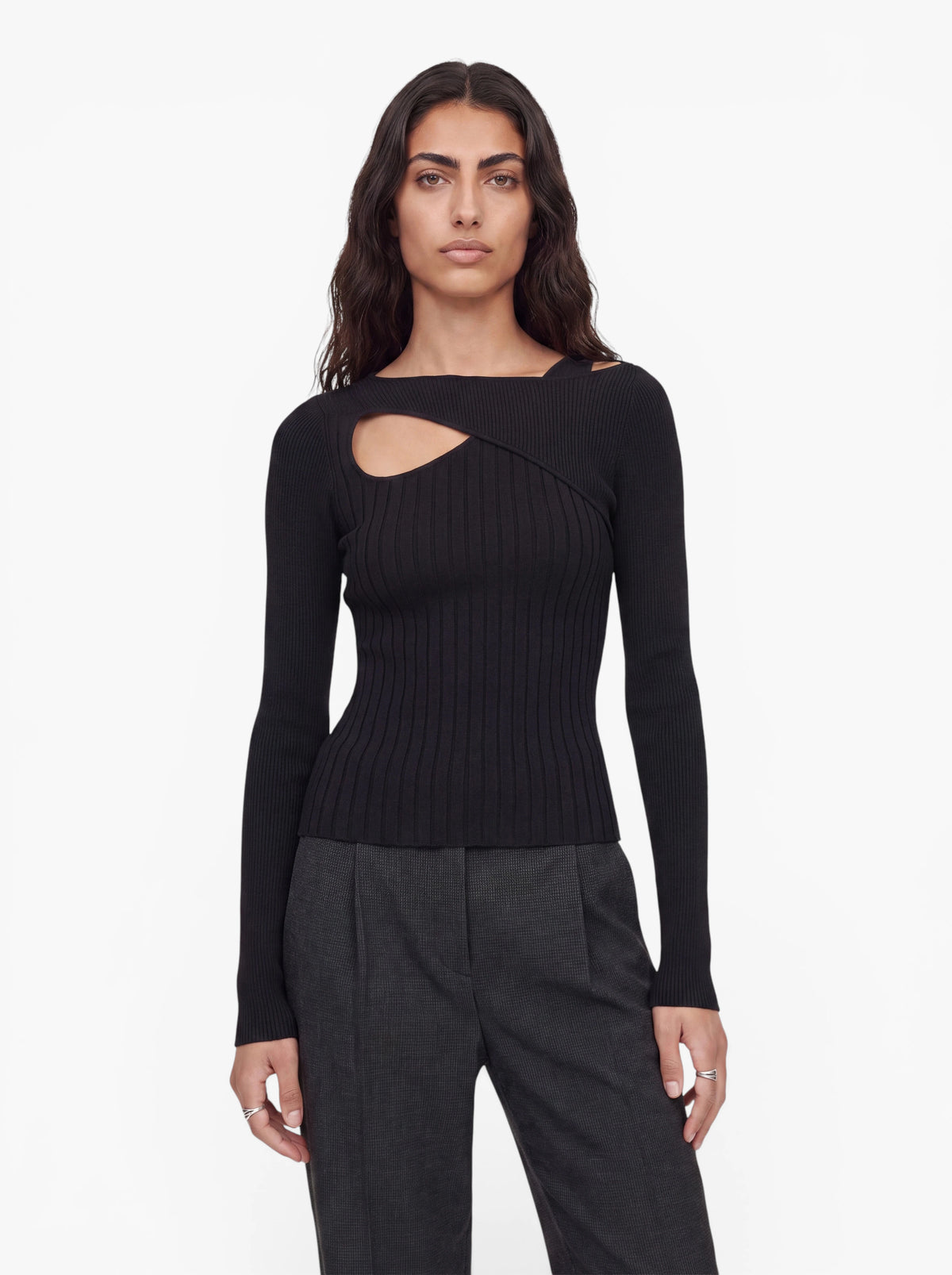 Eine Person mit langen, dunklen Haaren, die den Pullover „Selina“ von LeGer by Lena Gercke trägt – einen schwarzen Rippstrickpullover mit asymmetrischem Ausschnitt –, kombiniert mit einer grauen Hose, steht mit dem Gesicht nach vorne vor einem schlichten weißen Hintergrund.
