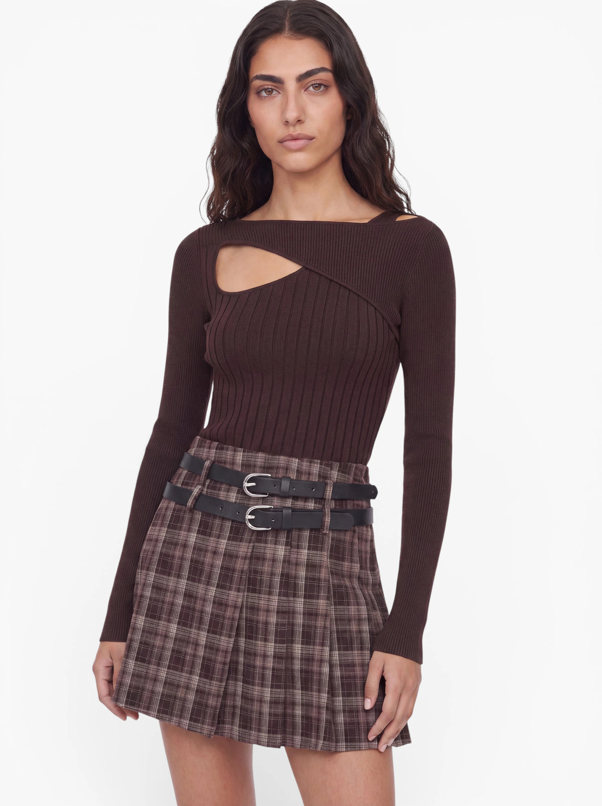 Eine Person mit langen, welligen Haaren trägt den Pullover „Selina“ von LeGer by Lena Gercke – einen olivgrünen Rippstrickpullover mit asymmetrischem Ausschnitt –, kombiniert mit einem braunen, karierten Faltenrock mit zwei schwarzen Gürteln, vor einem schlichten weißen Hintergrund.