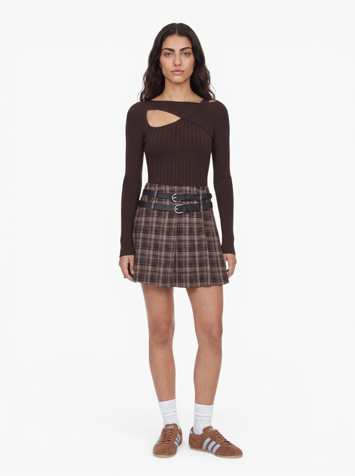Eine Person steht mit dem Gesicht nach vorne und trägt den Pullover „Selina“ von LeGer by Lena Gercke – ein olivgrünes Top mit Cut-outs und asymmetrischem Ausschnitt –, dazu einen karierten Faltenrock, einen Gürtel mit zwei Schnallen, weiße Socken und braune Sneaker mit hellblauen Streifen. Der Hintergrund ist schlicht weiß.