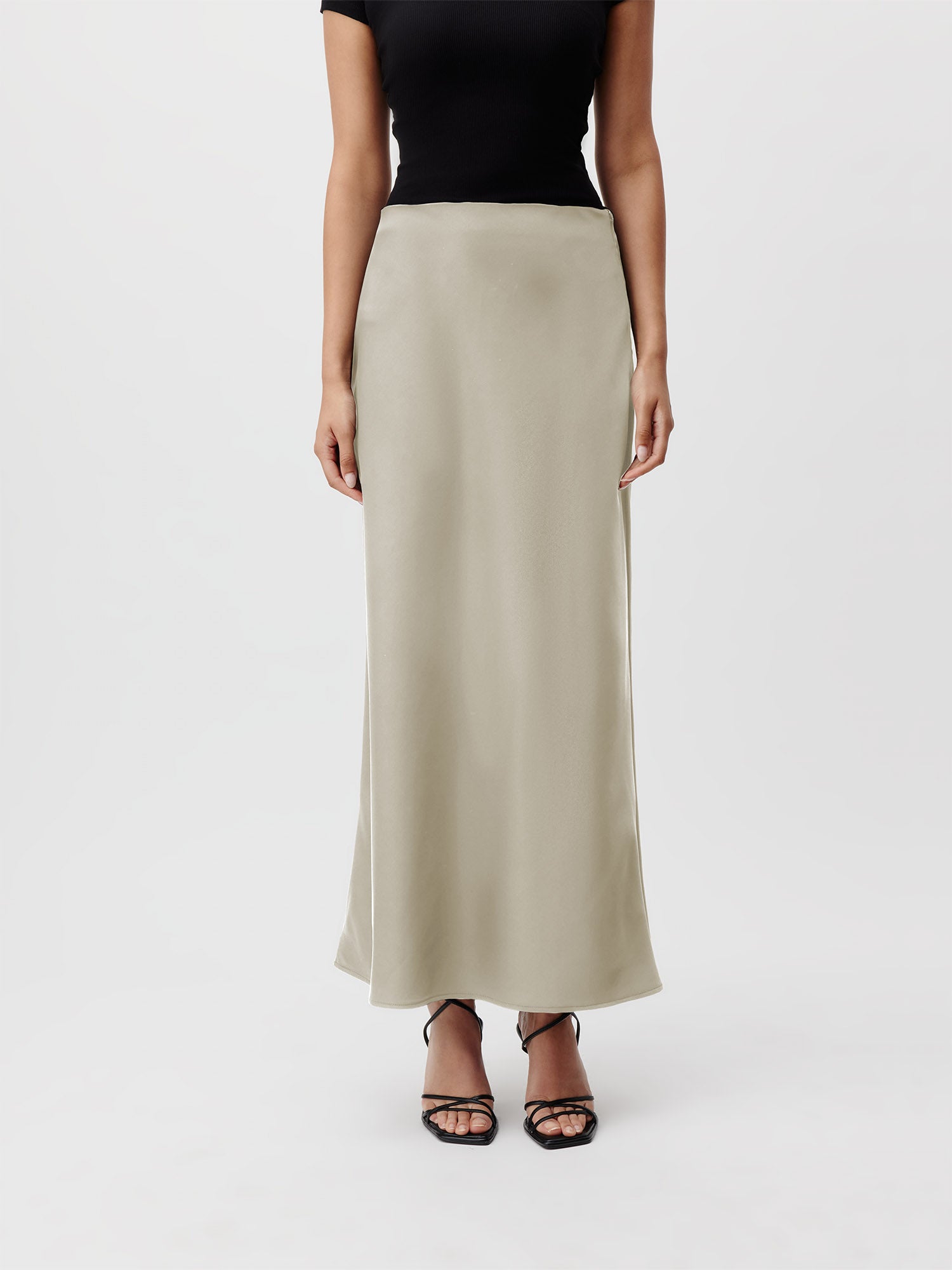 Eine Person steht vor einem schlichten Hintergrund und trägt ein kurzärmliges schwarzes Oberteil, das die Ärmellänge betont, einen knöchellangen hellgrauen Ida-Rock in Größe 36 von LeGer by Lena Gercke und schwarze Riemchen-Pumps. Der Kopf der Person ist im Bild nicht sichtbar.