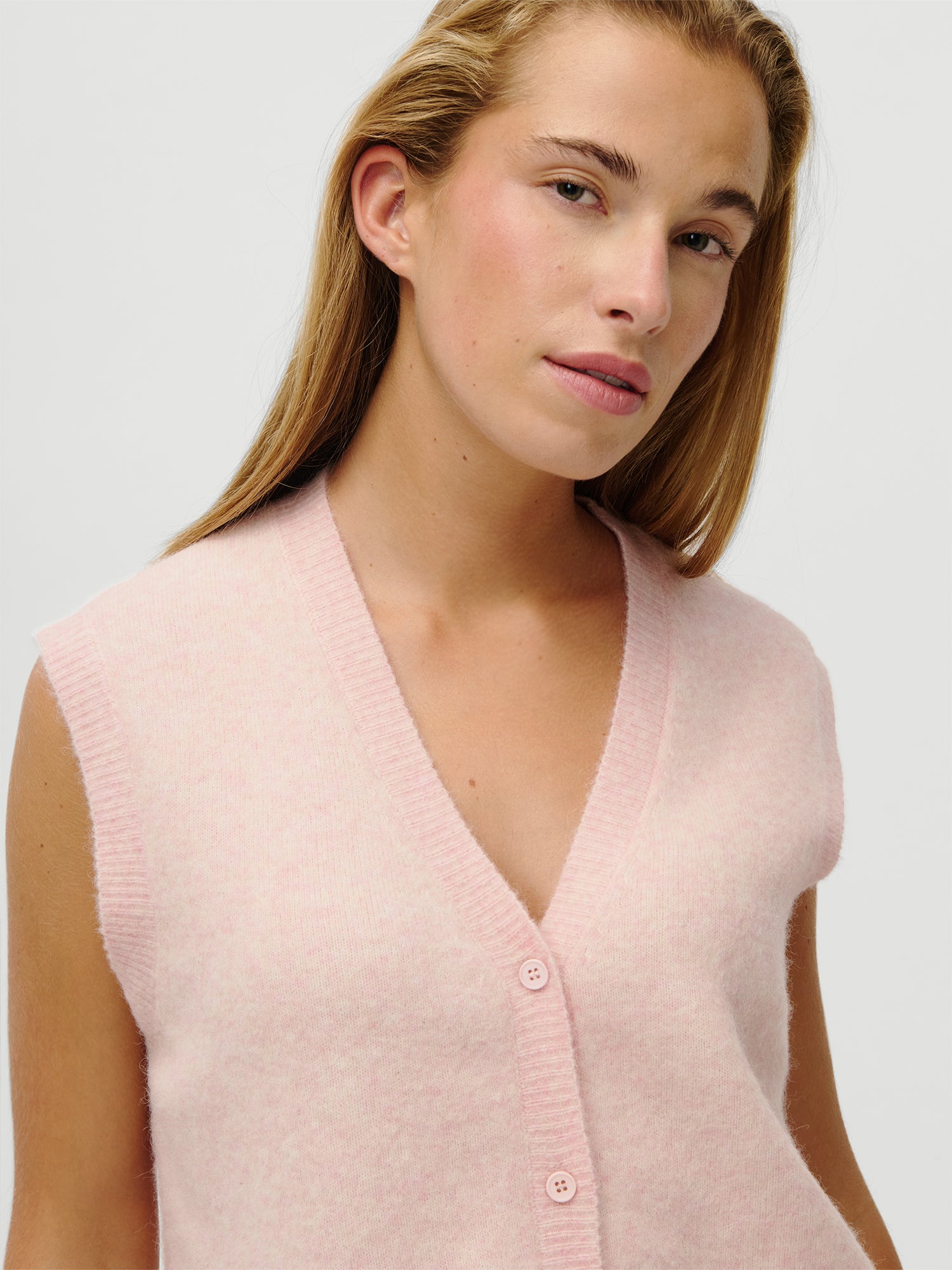 Eine Person mit langen blonden Haaren trägt die LeGer x Oh April - Amira Knit Vest von LeGer by Lena Gercke in Größe 36, mit einem ärmellosen, hellrosa Fuzzy-Design mit Knöpfen und einem V-Ausschnitt. Das Model ist 1,73 m groß, Passform: normal, abgebildet vor einem schlichten hellen Hintergrund.